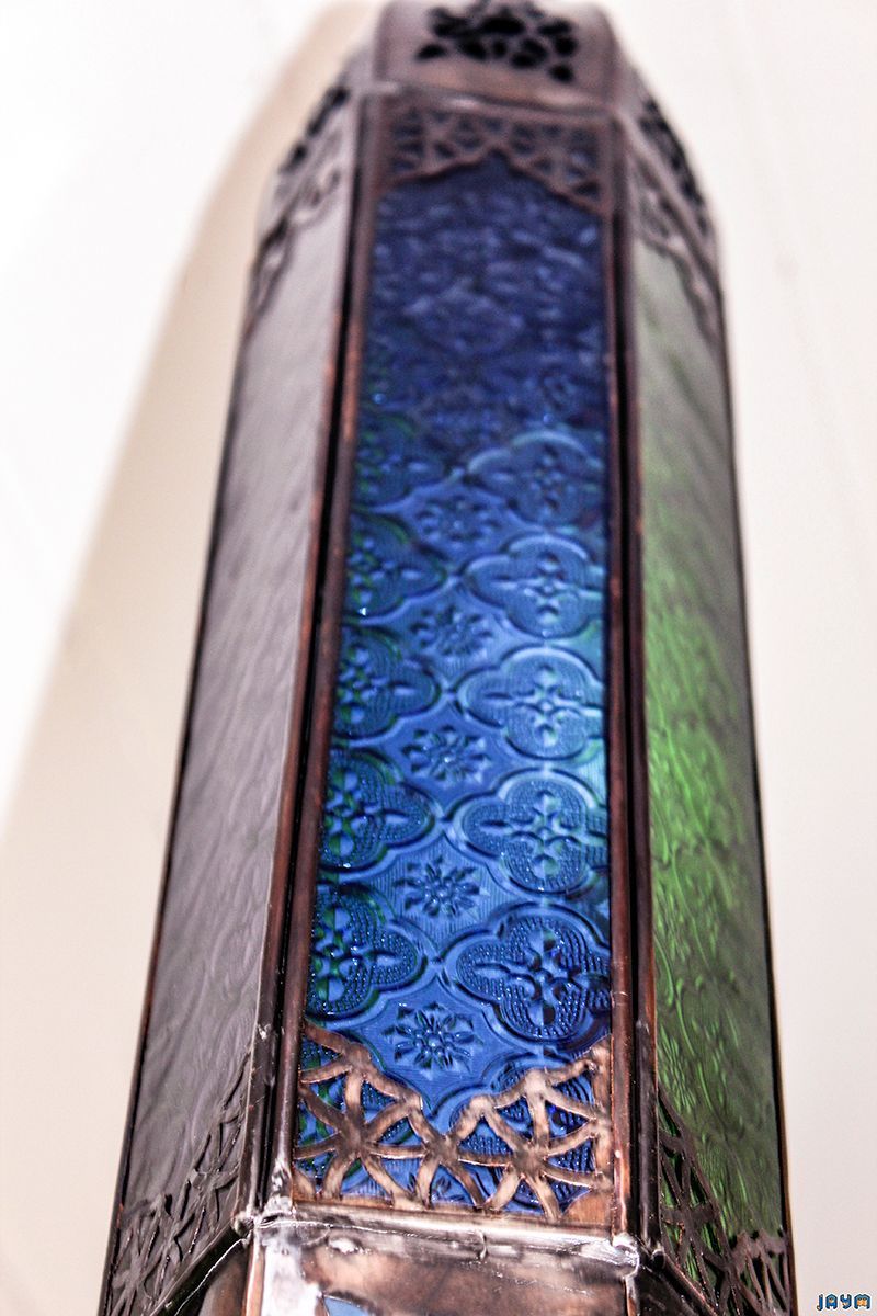 Zoom sur les panneaux de verre bleu d'un luminaire de style mauresque, encadrés par une structure métallique finement découpée.