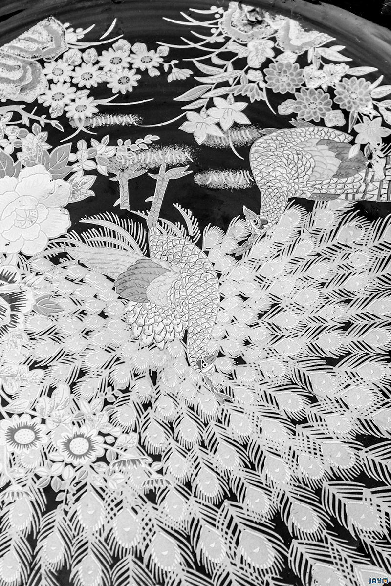 Détail d'un plat traditionnel aux couleurs vives représentant deux paons au plumage doré et turquoise entourés de fleurs de lotus et de pivoines sur un fond noir.