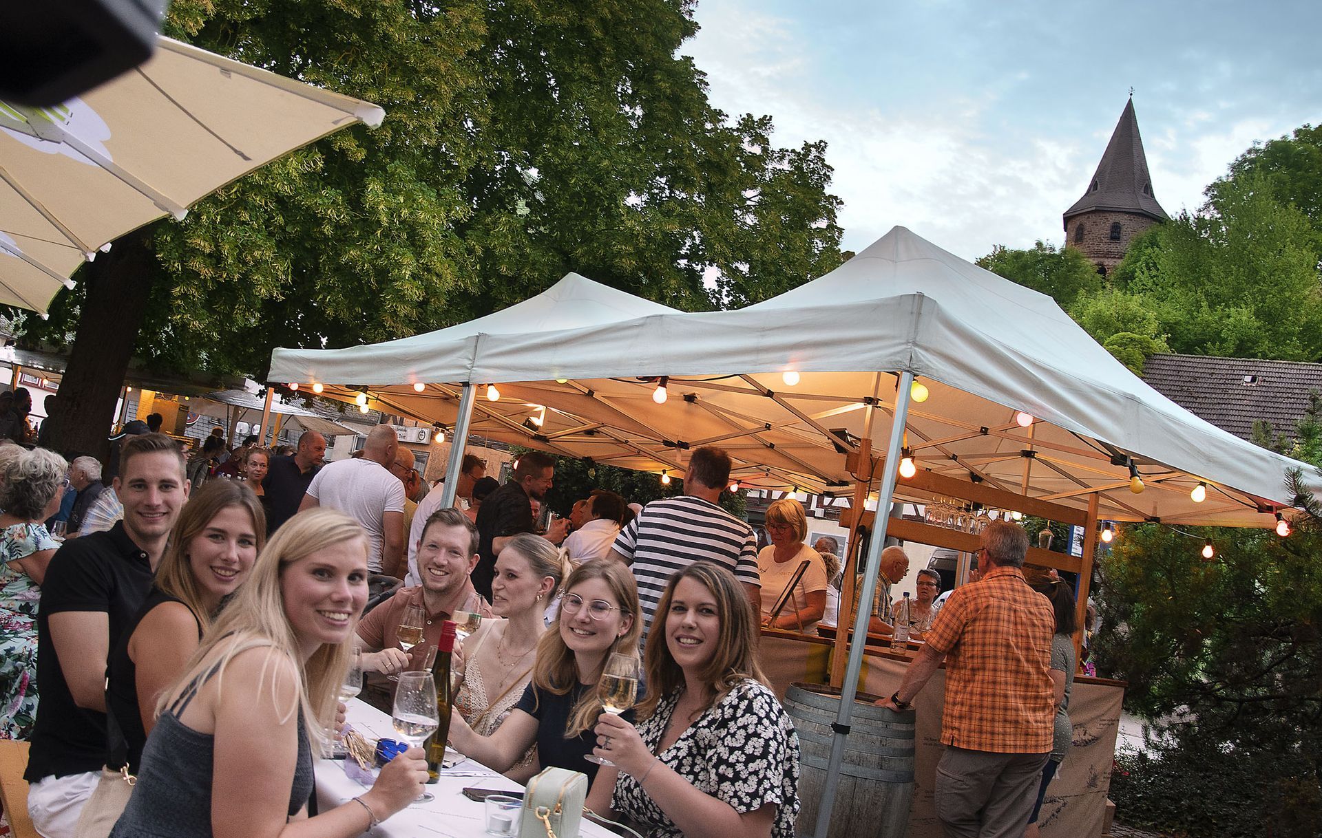 Menschen genießen einen Wein auf dem Rathausplatz während des Weinfestes 2023. Im Hintergrund der Kirbergrturm.
