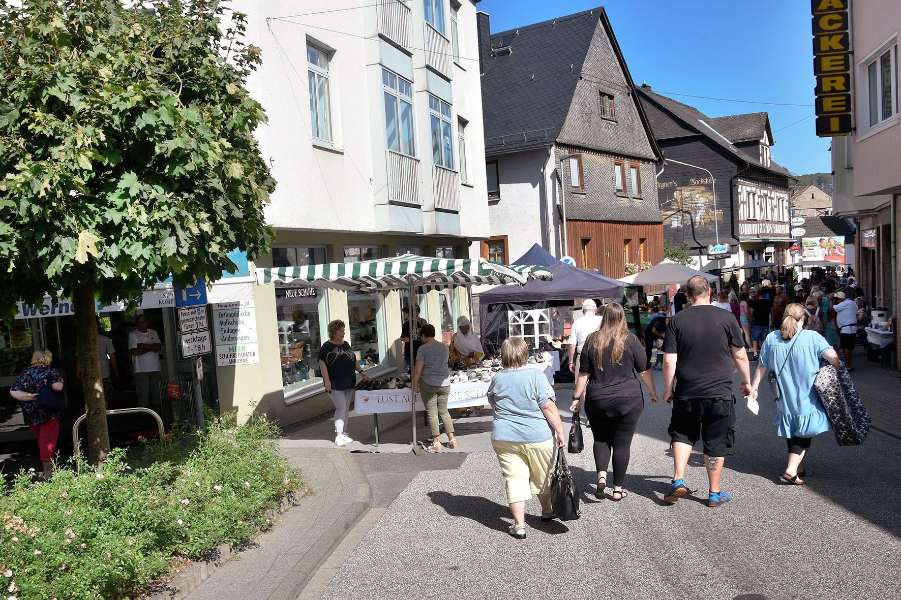 Bauernmarkt in der Hauptstraße in Weilmünster mit dem Schuhfachgeschäft, mehreren Verkaufsständen und Menschen., die dort entlang gehen.