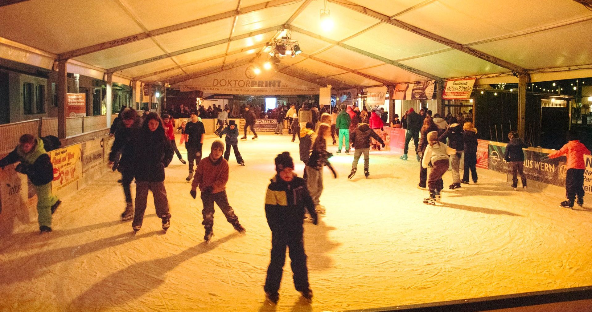 Die überdachte Schlittschuhbahn auf dem Marktplatz Weilmünster voller Kinder und Jugendlicher beim Eislaufen.