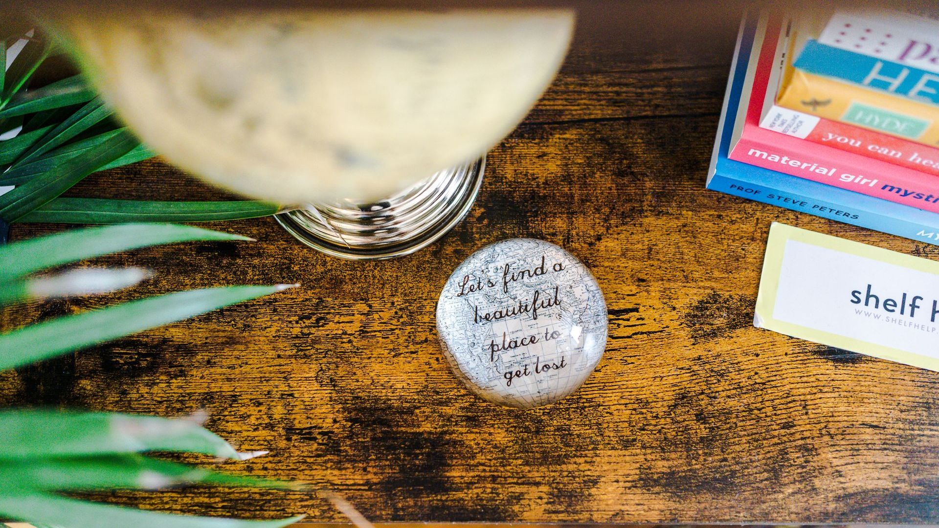 bookshelf with a globe of the world and paper weight saying 'lets find a beautiful place to get lost'