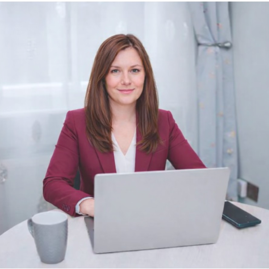 women in red business suit sat at dining table with laptop