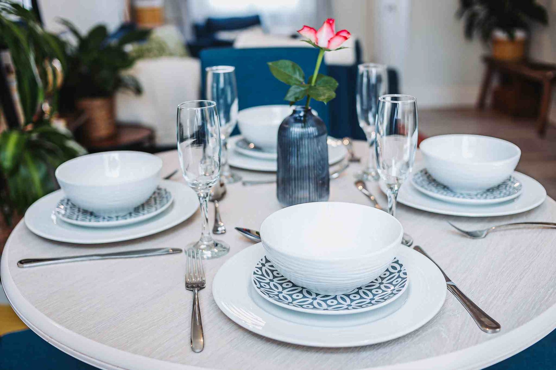 dining table set up with white and blue crockery and central rose in blue vase