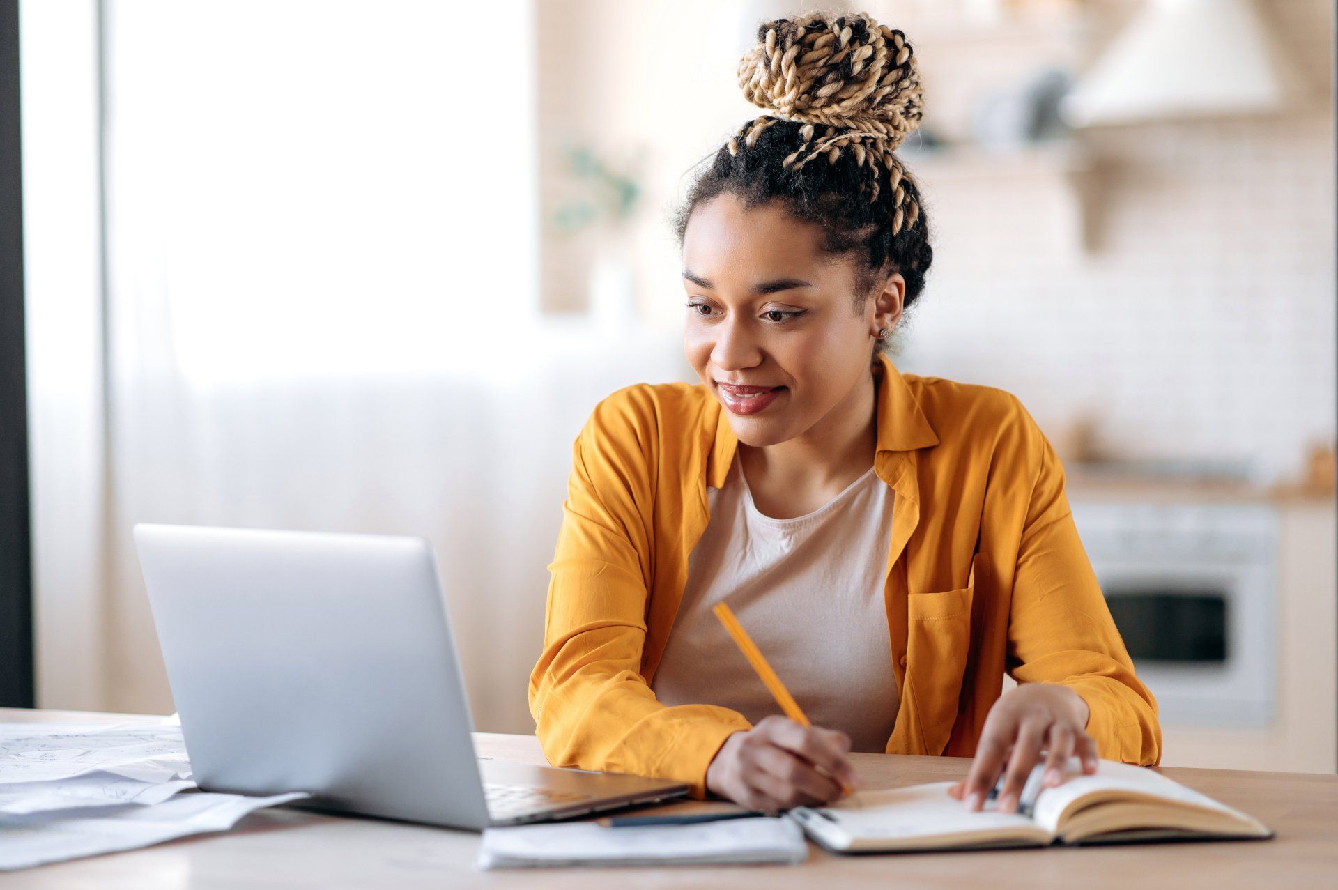 Jeune femme à un bureau souriant face à un ordinateur et écrivant sur un cahier