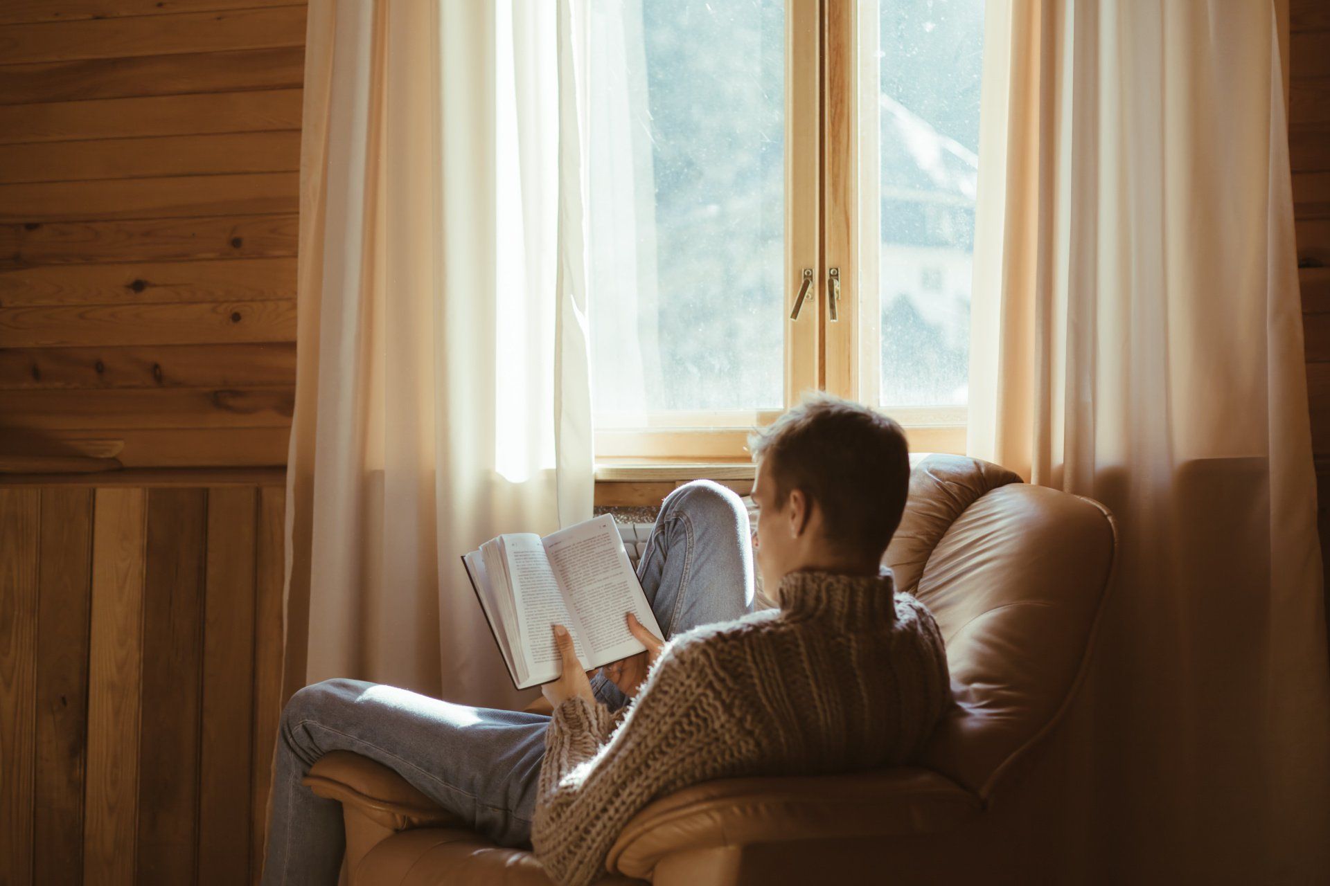 Homme lisant un livre dans son canapé face à une fenêtre