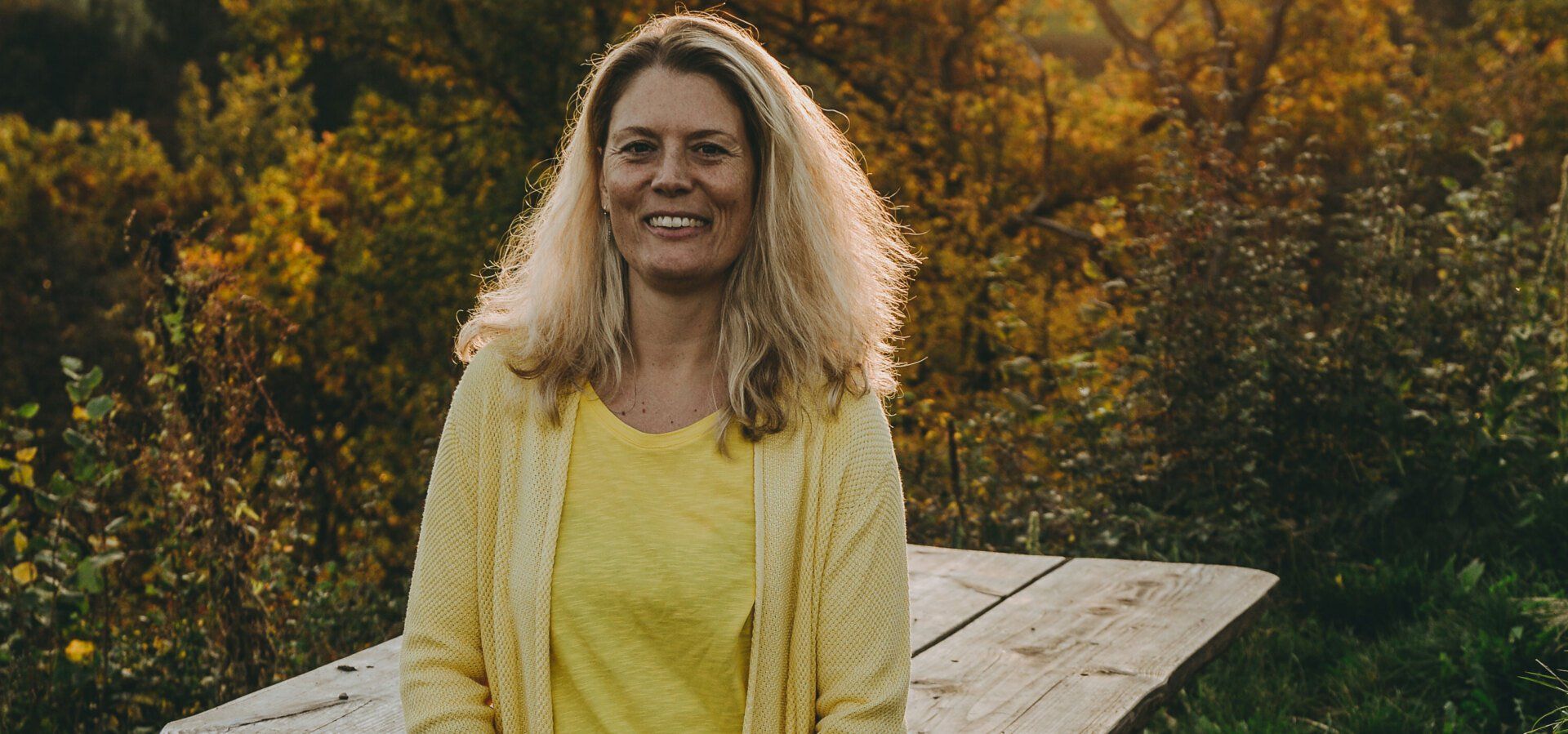 Frau mit langem Haar leht an Holztisch im Herbstwald