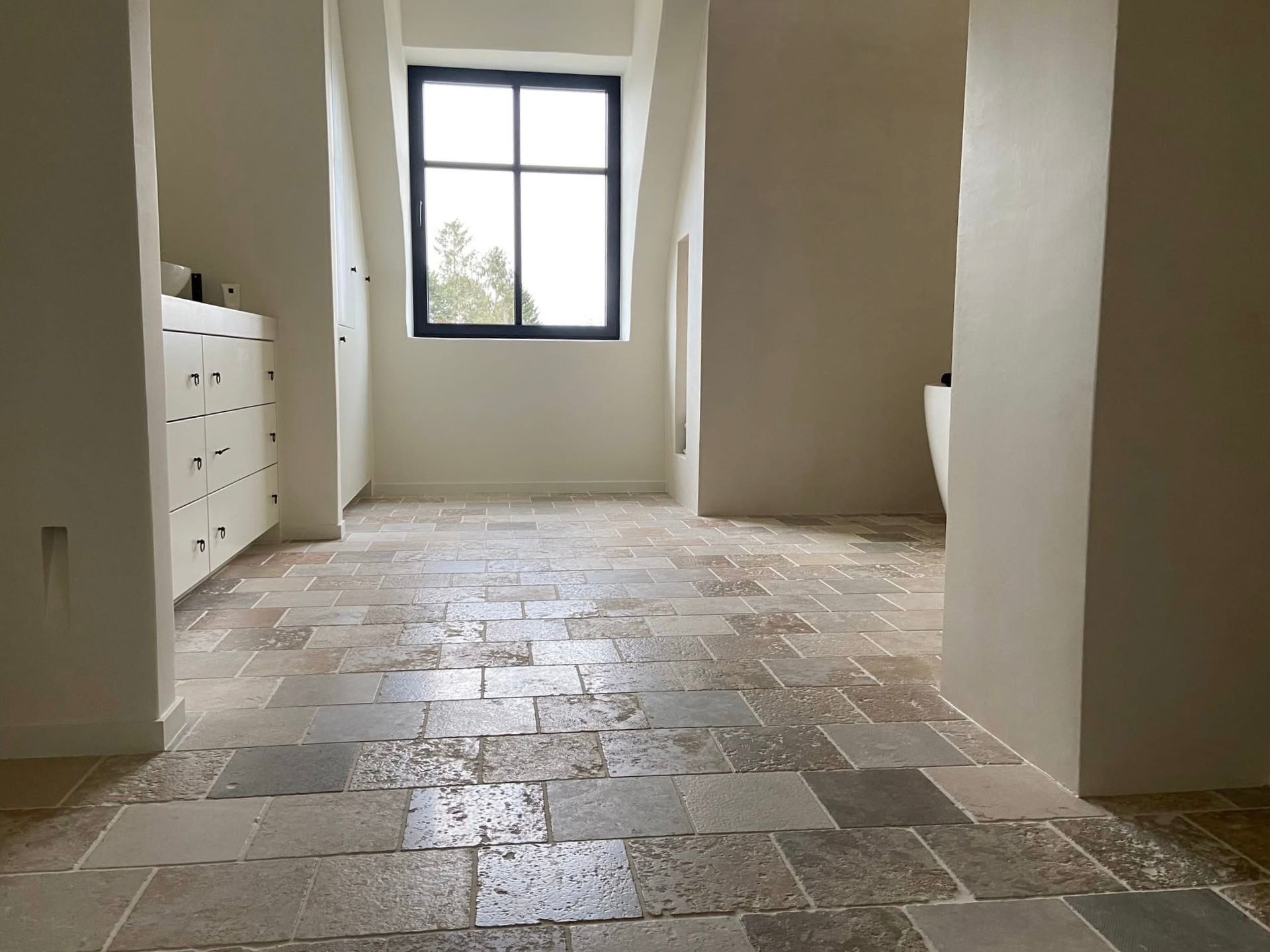 Moderne Architektur mit kleinformatigen Natursteinfliesen, weißer Wachtisch mit Unterschrank und runde Badewanne