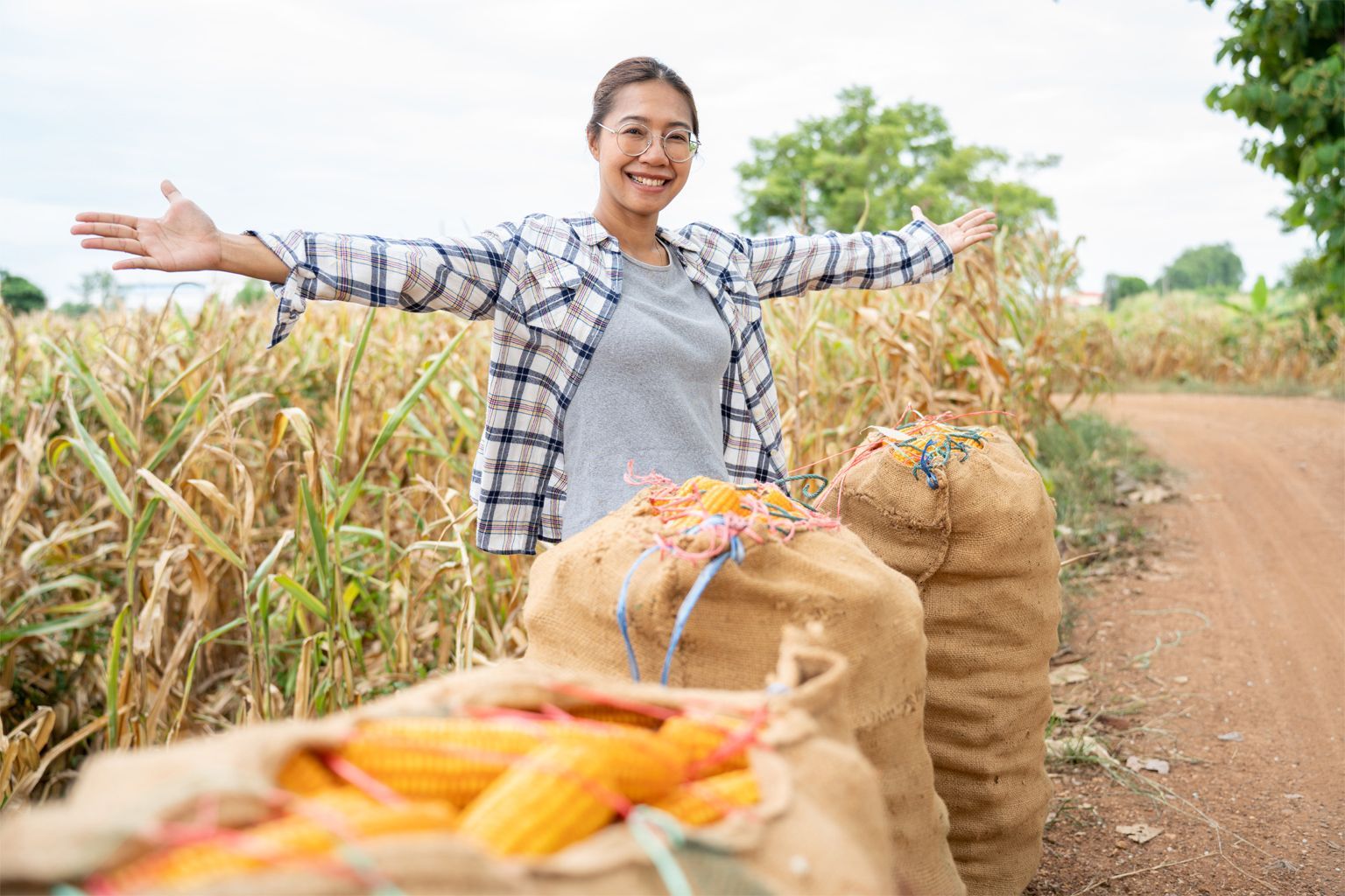A woman celebrating harvesting a large quantity of corn in 3harvest bags.