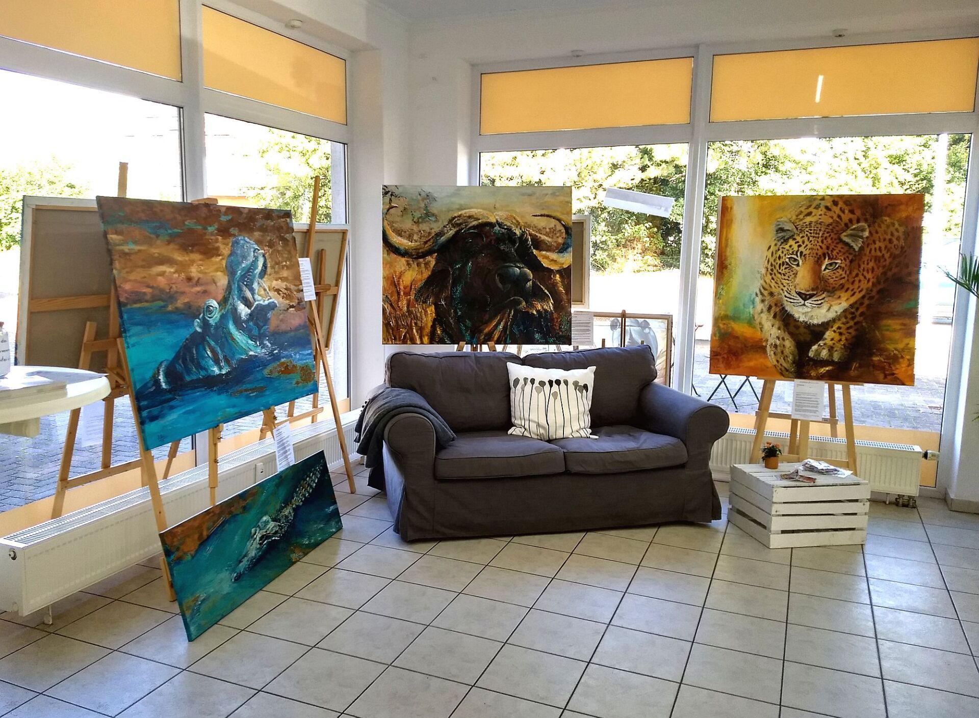 Sitzecke im Galerieatelier von Bianca Leidner mit gemütlichem Sofa und Gemälden von Nilpferd, afrikanischem Büffel, Leopard und Krokodil im Hintergrund