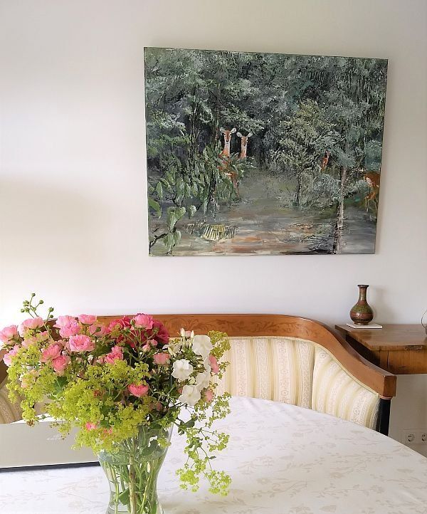 Bild mit Buschböcken  an einer Wand, davor ein Sofa und ein Tisch auf den ein schöner Blumenstrauß steht. Überwiegende farben: grün, braun, beige, rosa