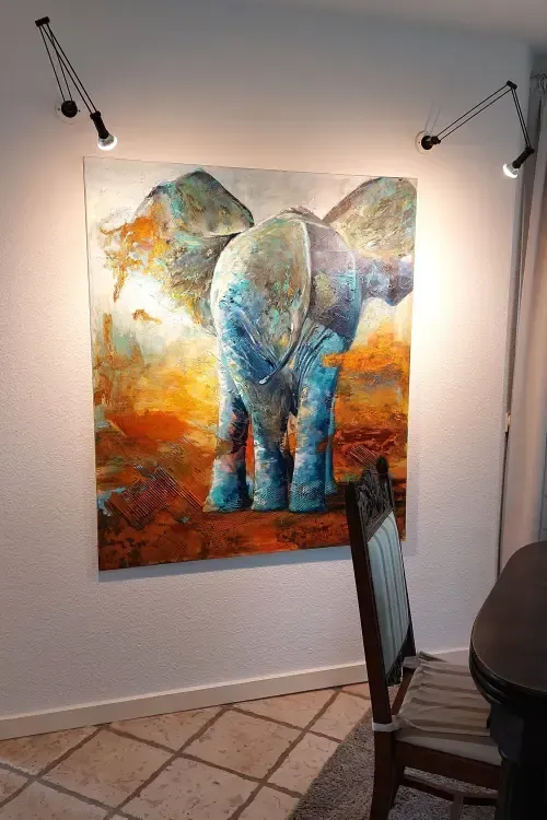 Gemälde eines Elefanten von hinten in Blau-türkistönen und Sienna, das leuchtend angestrahlt an einer Wand hängt