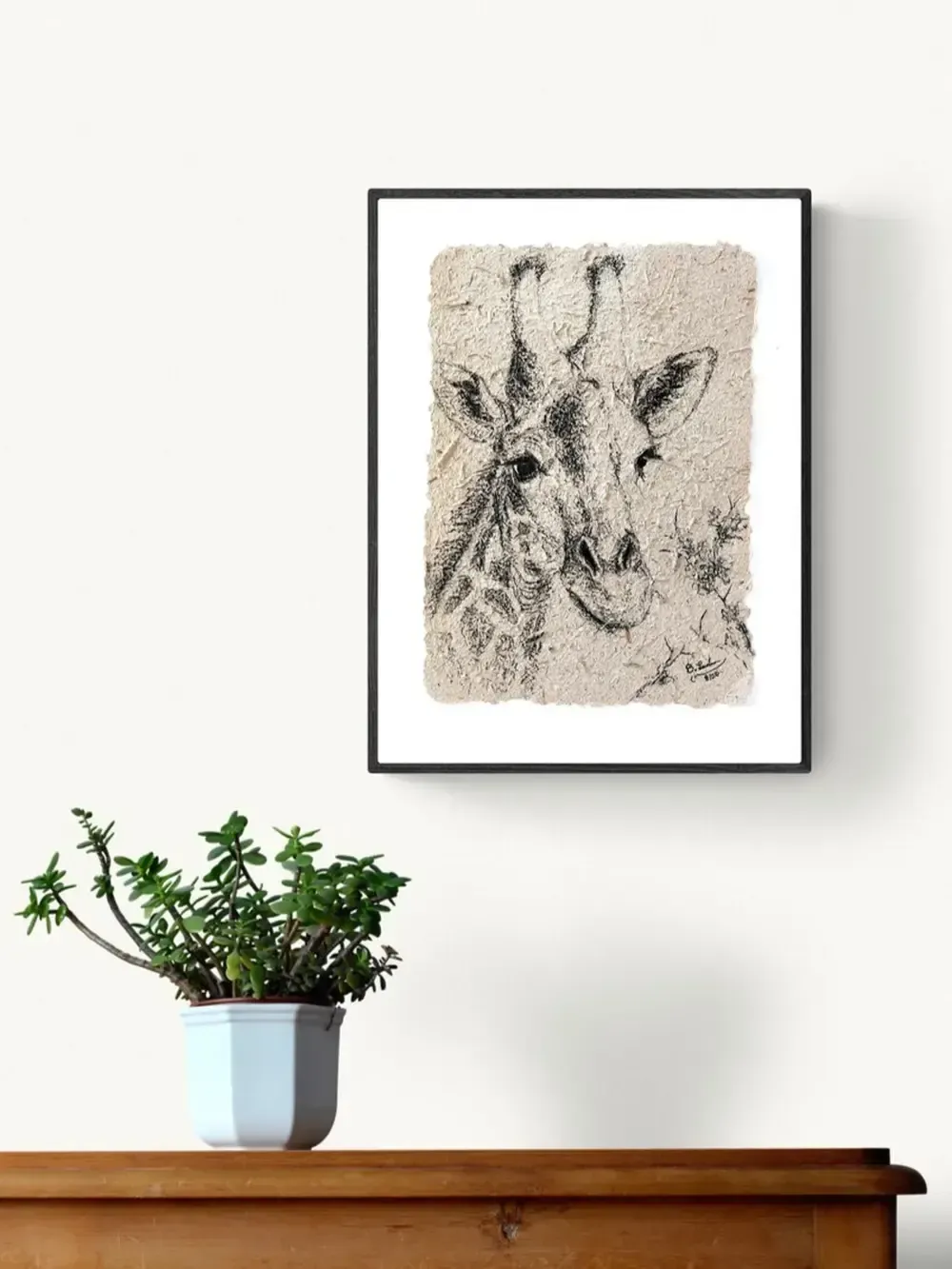 gerahntes Portrait einer Griraffe mit Kohle auf Elefantenpapier gezeichnet, das aus Elefantendung in Uganda hergestellt wurde. Es hängt an der Wand über einer Komode