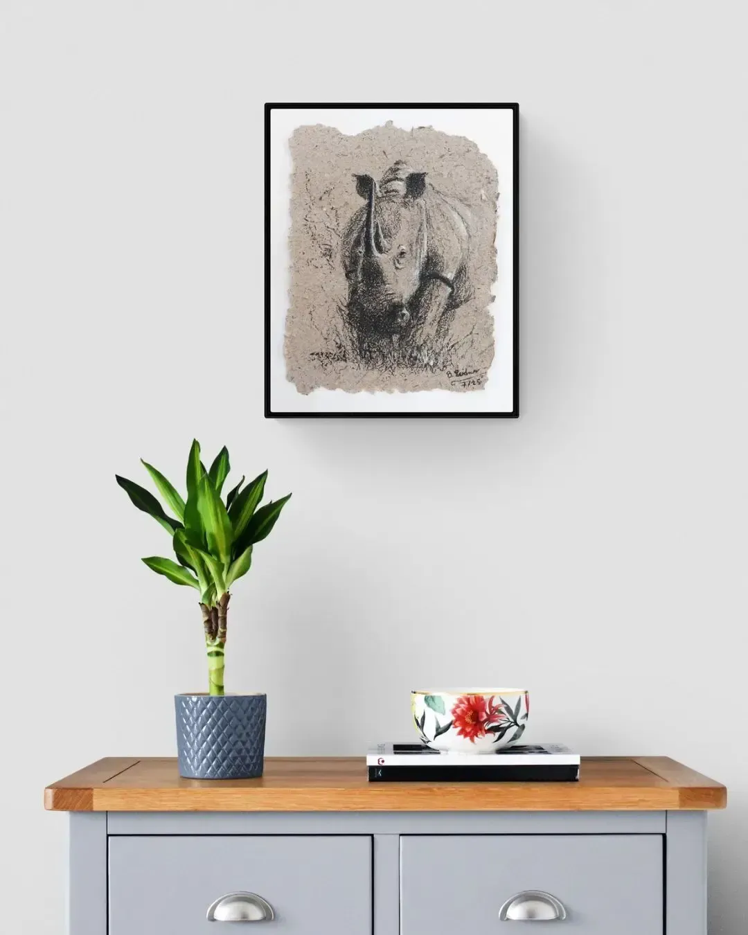 Nashornmama mit Kohle auf Elefantenpapier gerahmt an der Wand über einer Komode