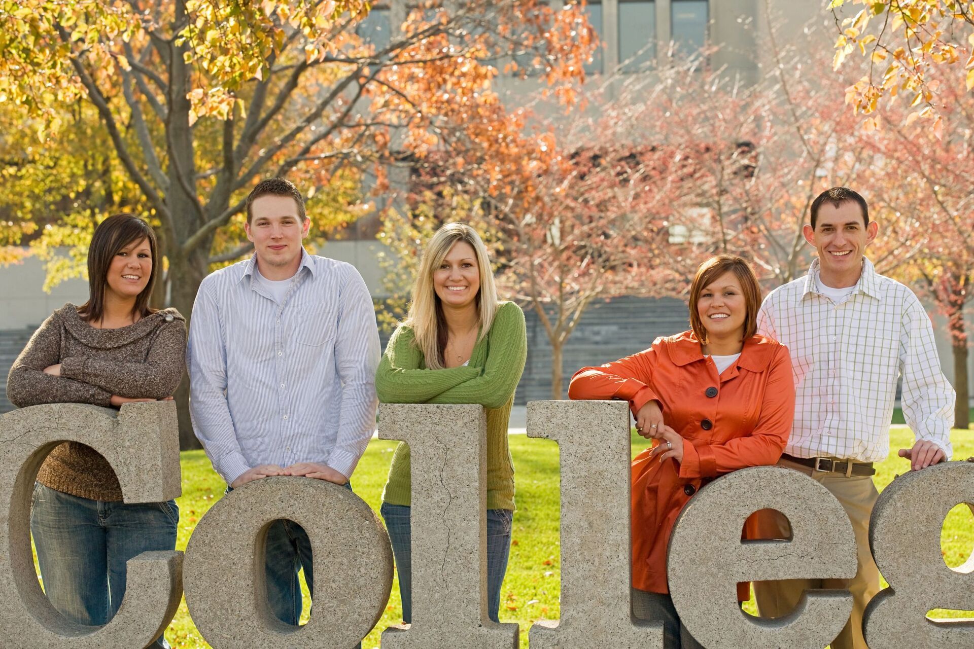 Parents standing with their children behind a college logo on a college campus tour.