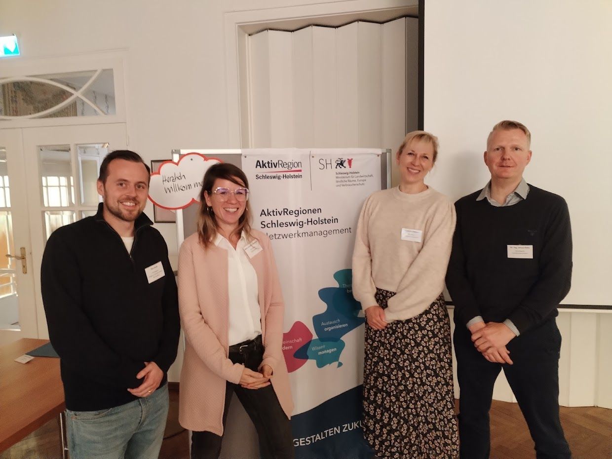 vier Personen, die in die Kamera lächeln, vor einer Karte vier Personen, die in die Kamera lächeln, vor einer Karte