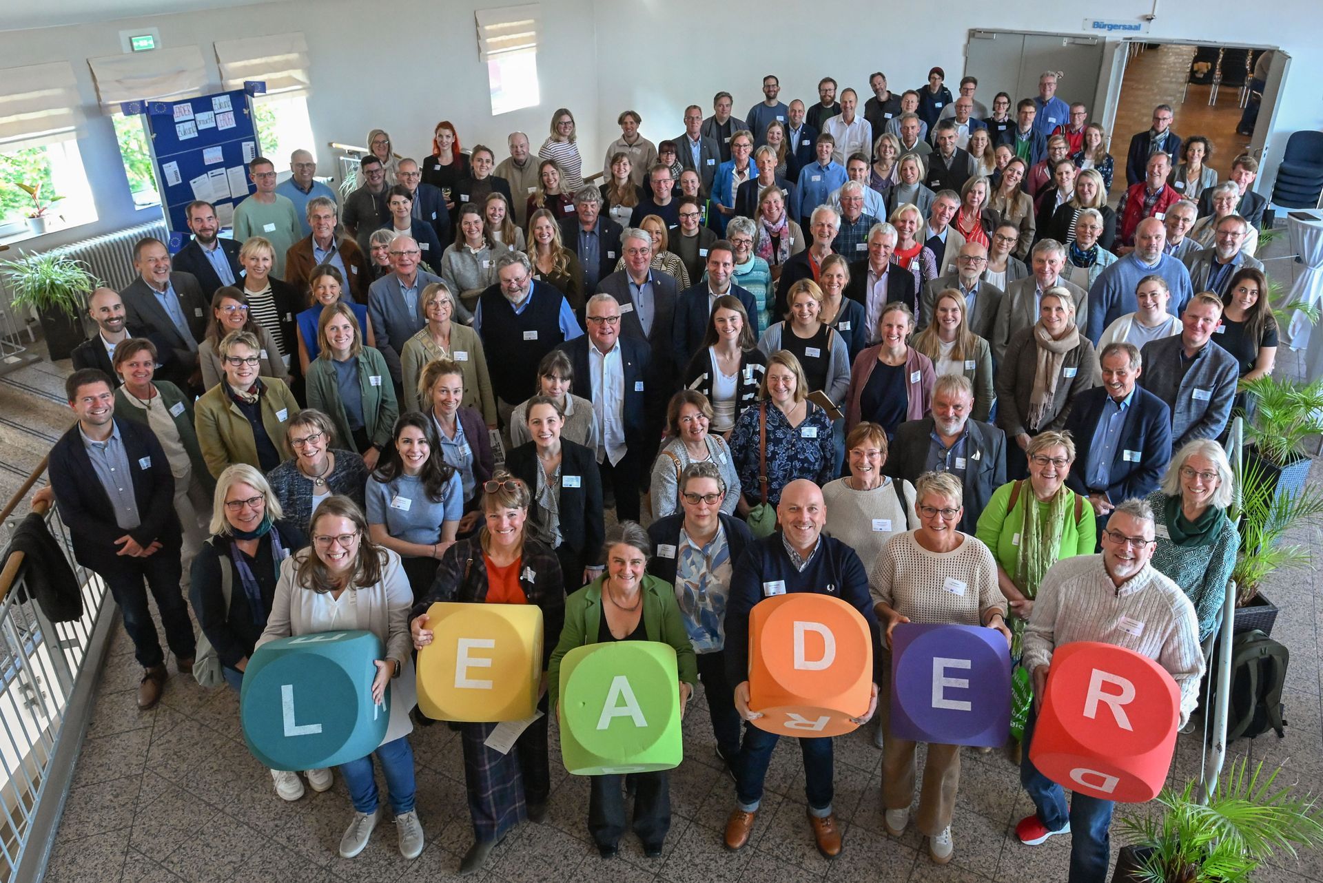 Ministerpräsident Daniel Günther umringt von drei weiteren Personen vor einem Grill Gruppenfoto der Veranstaltung mit dem Schriftzug LEADER im Vordergrund