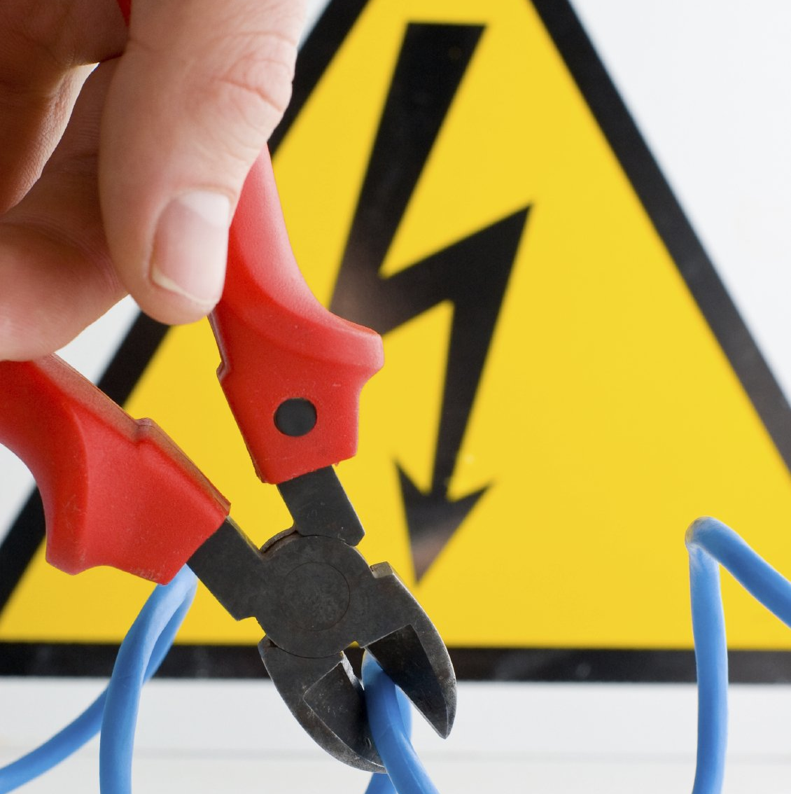 Gelbes Schild mit einem Blitz und davor ist ein blaues Kabel und eine Zange