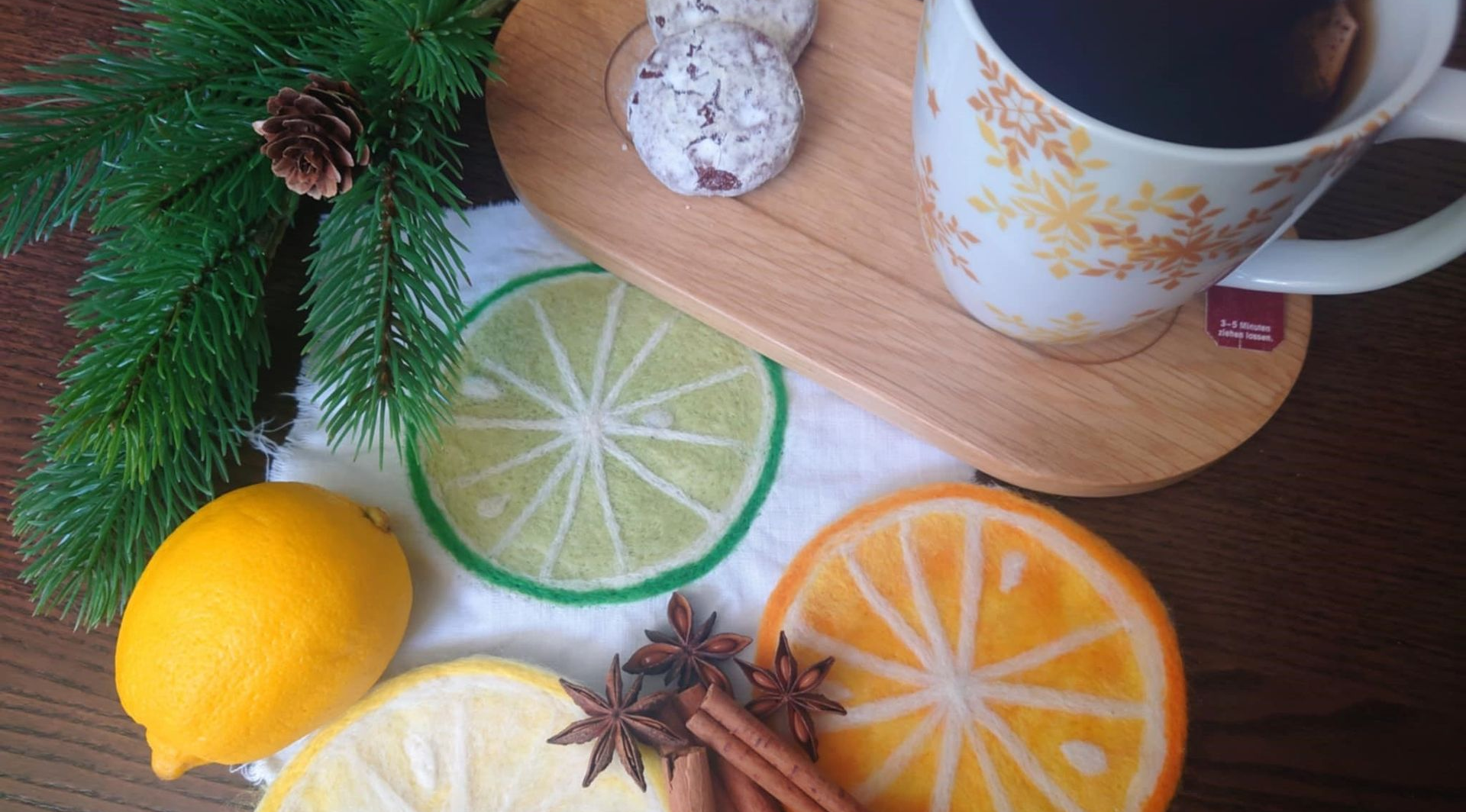 Weihnachtlicher Tisch mit einer Tasse, Lebkuchen und einer Zitrone, unterhalb liegen Untersetzer in Form von Zitrusfrüchten