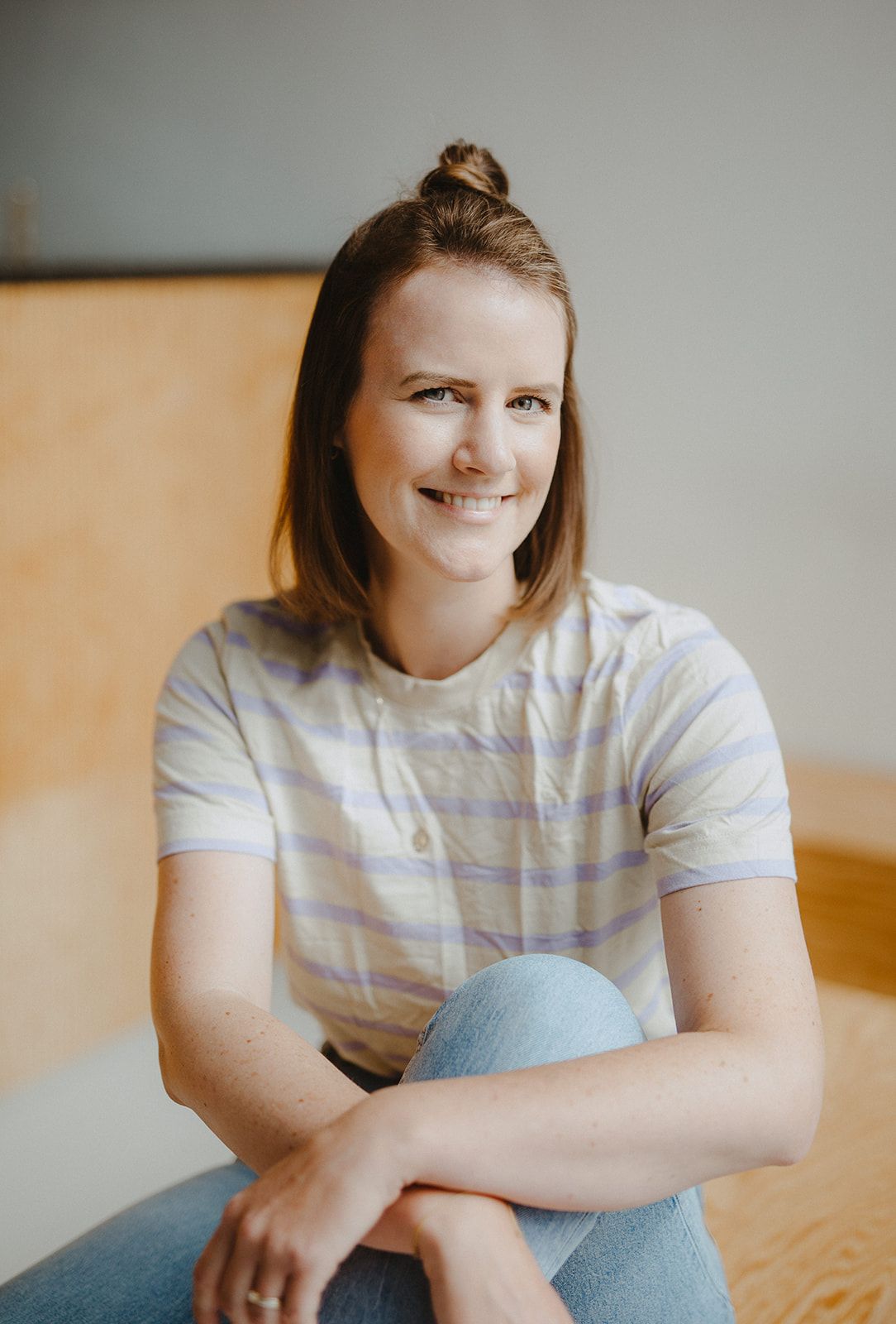 Deine SEO Coachin Anna Frau mit braunen Haaren und lila gelb gestreiftem T-Shirt sitzt mit verschränkten Armen und lächelt ins Bild