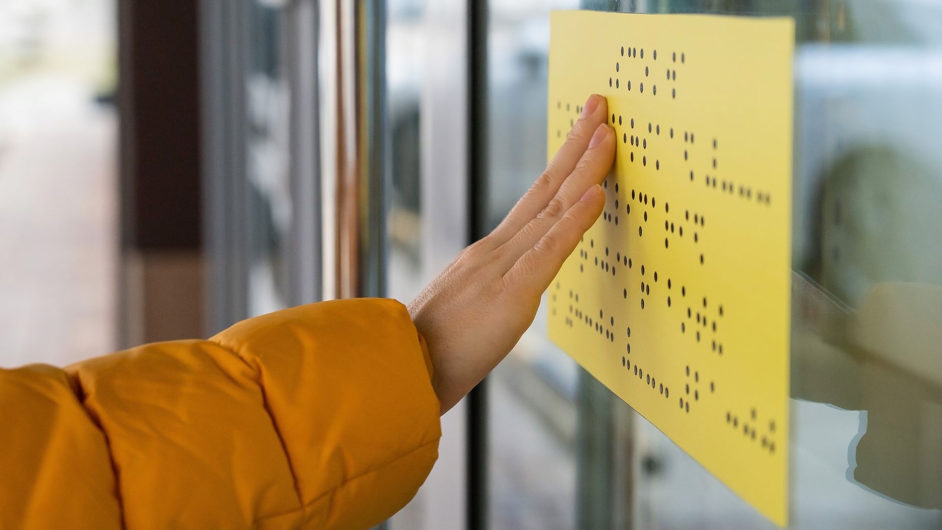 
Zu sehen ist ein Arm einer Person. Sie ließt mit der Hand das Eingangsschild in Brailleschrift