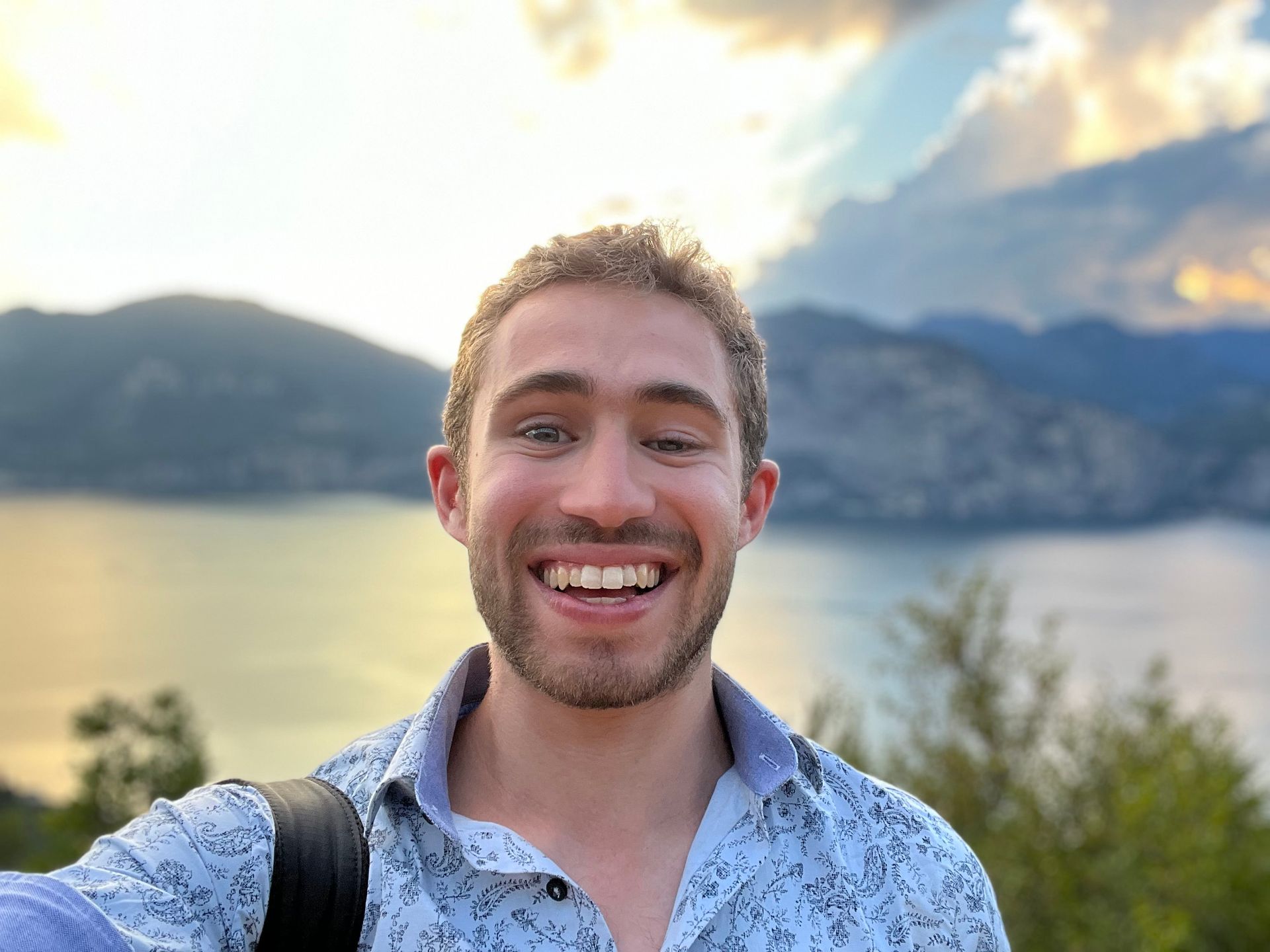 Austin Ali smiling at the camera with a natural scene of mountains and a river behind him.