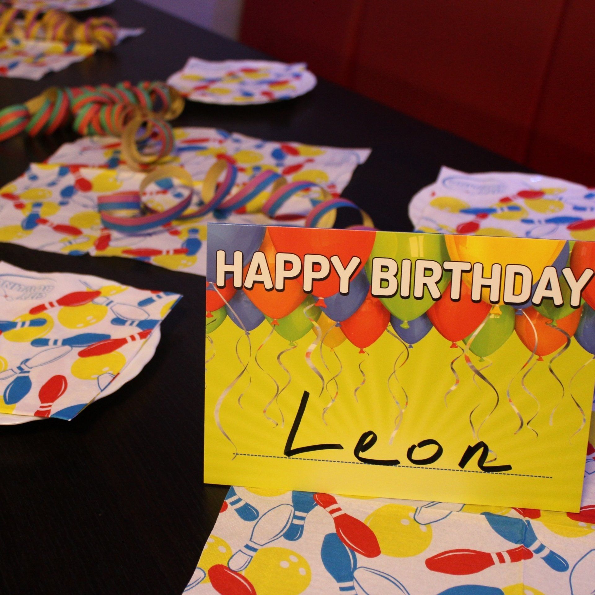 Geburtstagsfeiern für Kinder und Jugendliche in der City Bowling Kassel Bild Ausschnitt eingedeckter Geburtstagstisch in der City Bowling mit Tellern, Geburtstagsservietten und Einladungskarte mit Namen des Geburtstagskindes