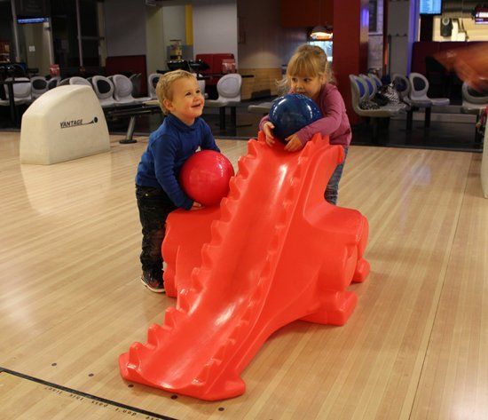 Bild mit Kinder auf der Bowlingbahn. Für die Ballabgabe benutzen sie eine Rampe in Form eines Dinos. Mit deren Hilfe können Kinder besser zielen.