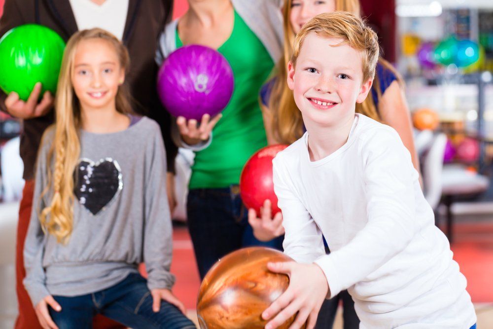 Kindergeburtstag im City Bowling Kassel Bild einer Familie die Bowling spielt. Eltern mit 2 Töchtern im Hintergrund, der Sohn vorne an der Bahn