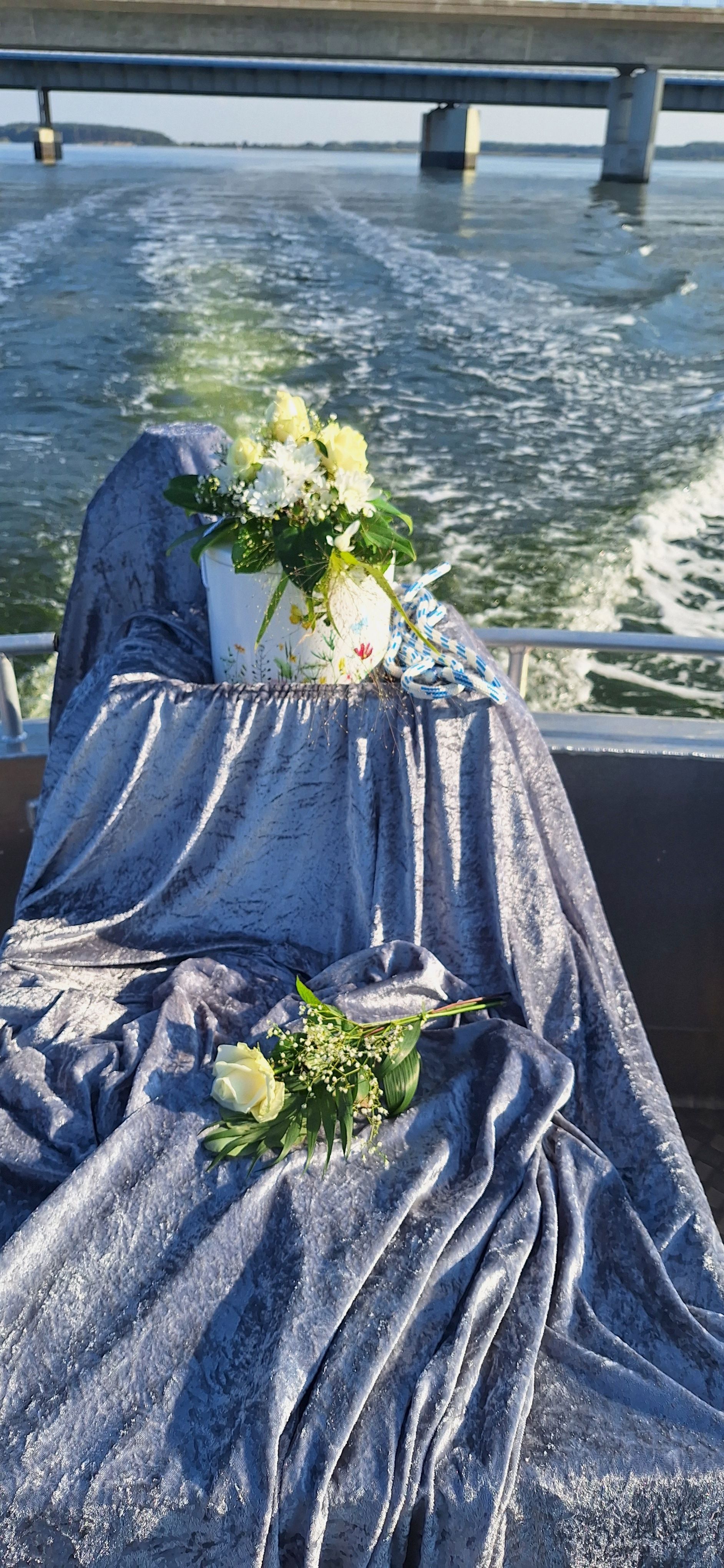Blauer Himmel mit einer Urne für die Seebestattung im Hintergrund das Boot Paula fährt gerade unter einer Brücke durch.