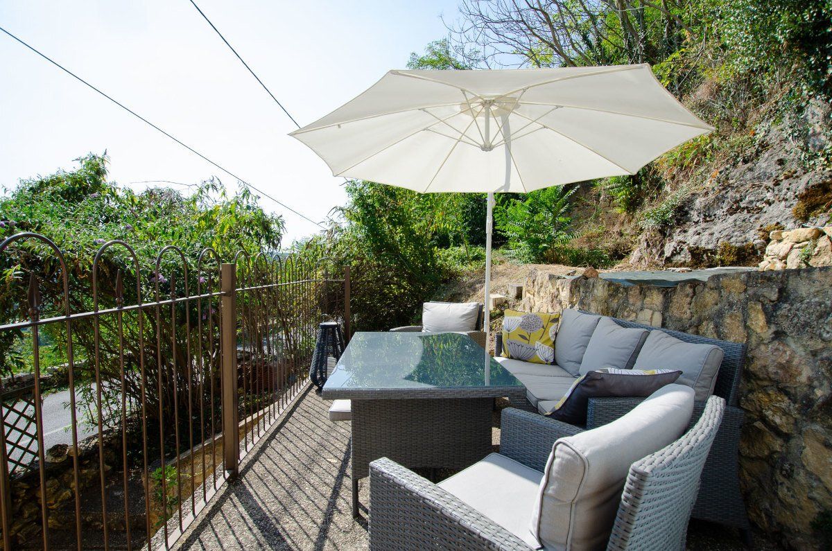 Terrasse de la Perle Noire, ensoleillée avec salon de jardin et parasol, au pied d'une falaise végétalisée dans le Périgord Noir