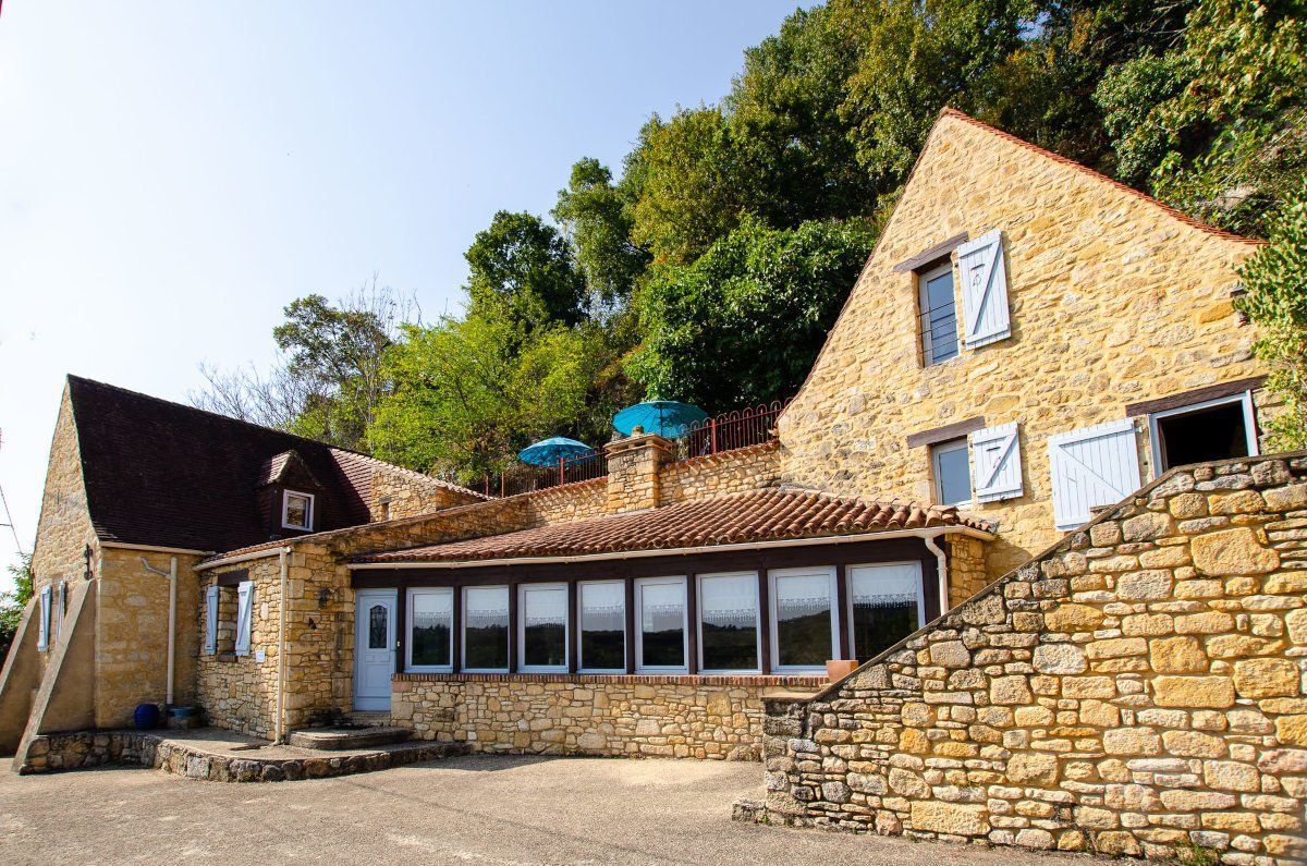 Maison en pierre typique du Périgord avec volets bleus, entourée de végétation