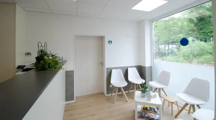 Unser heller Wartebereich im Therapiepunkt Eifel Heller Wartebereich der Physiotherapie Praxis Therapiepunkt Eifel. Weiße Stühle, Empfang und Logo der Praxis am Fenster.