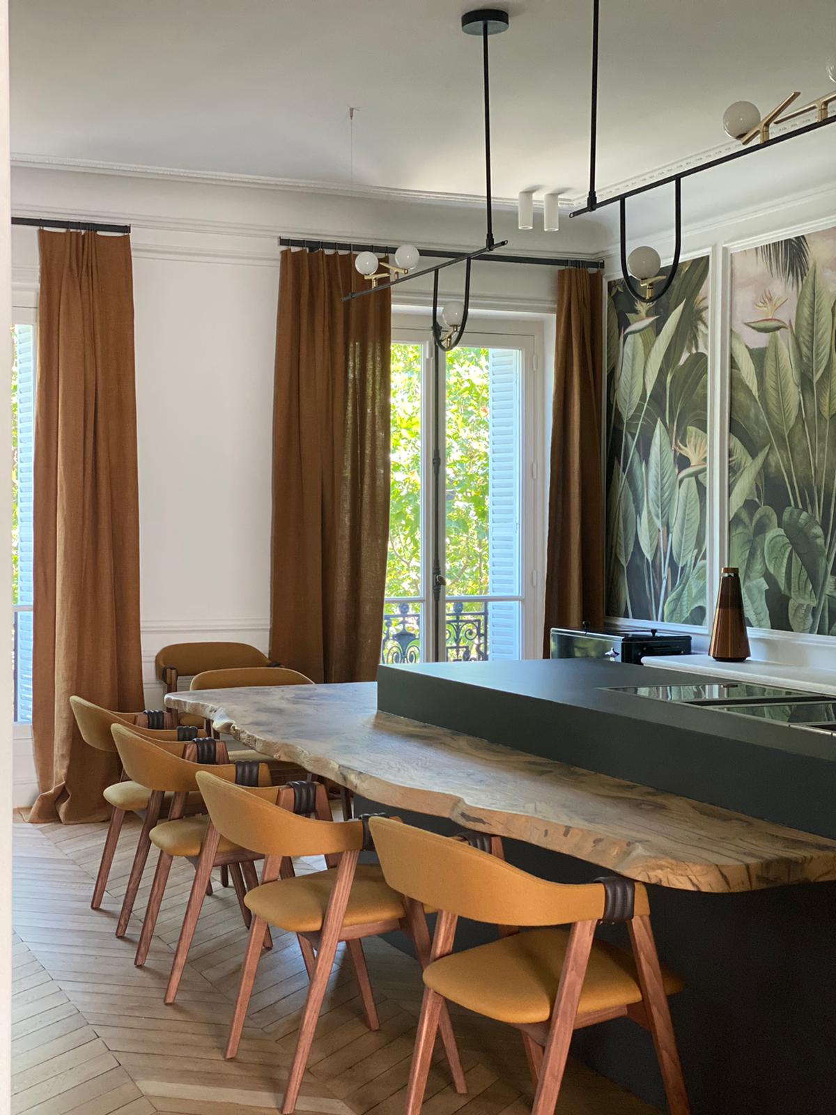 Table de bar en bois brut longeant subtilement un grand caisson de cuisine moderne.