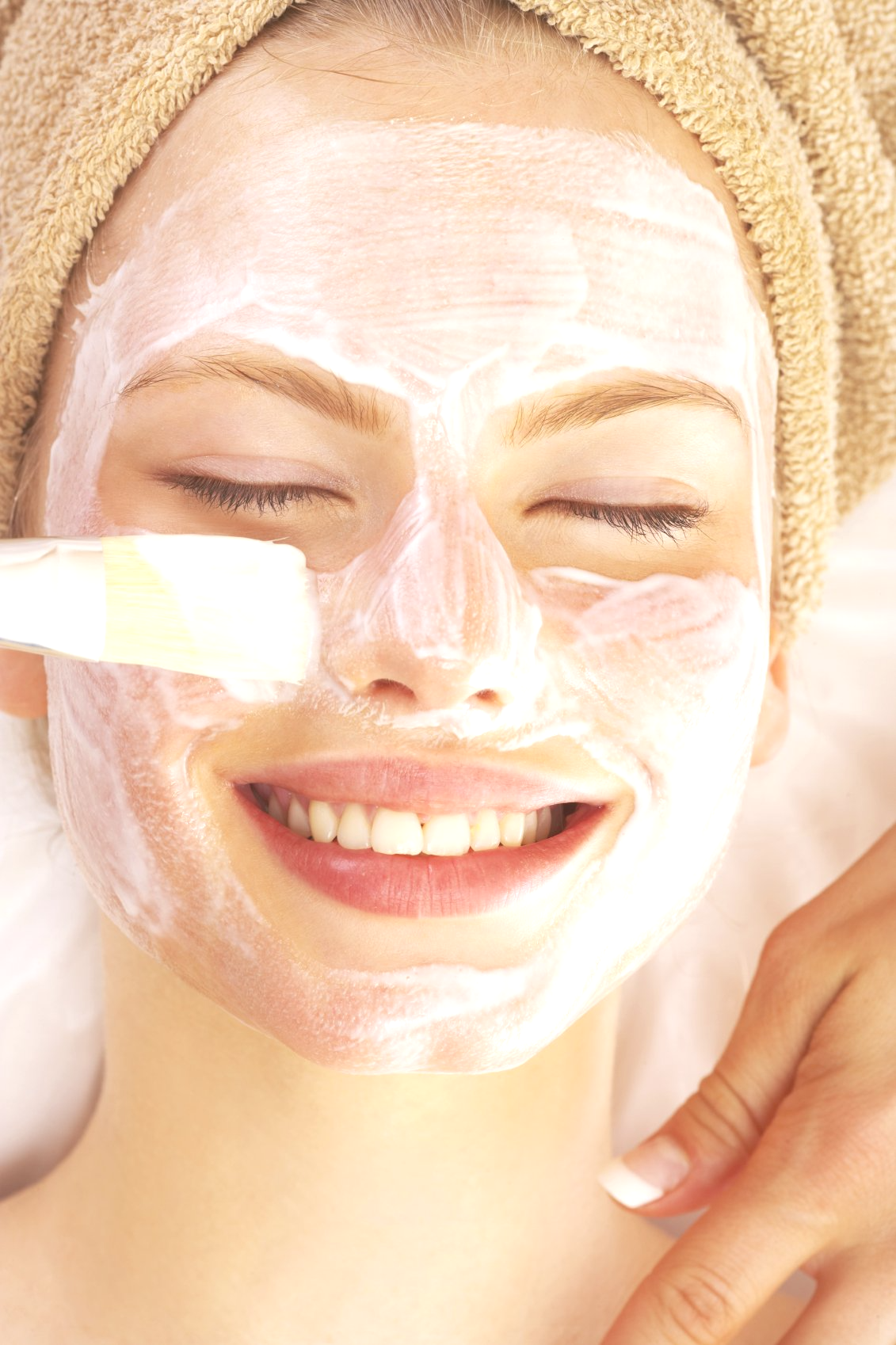 A young woman lying down smiling, enjoying a facial exfoliating treatment.