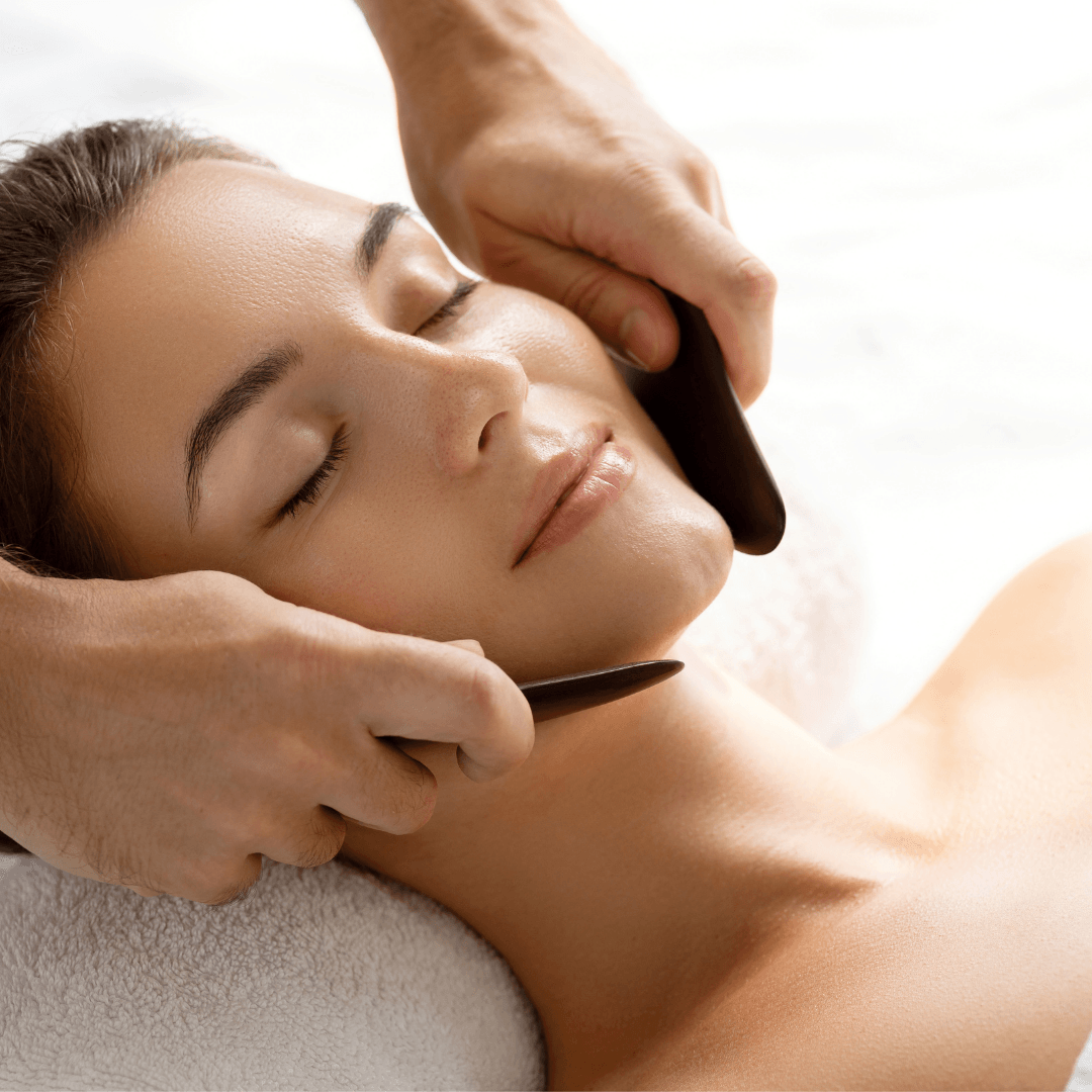 Woman lying down on a massage bed enjoying Gua Sha facial massage.