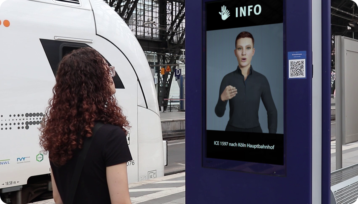 Frau steht vor einem Gebärdensprach-Avatar Terminal am Bahnhof