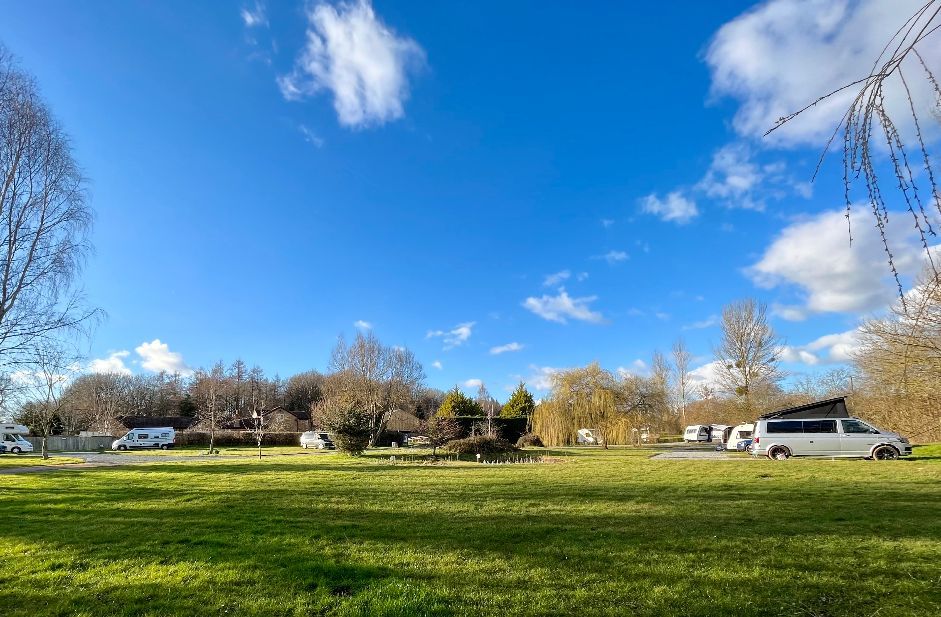 Meadow brook field full of campervans, with hardstanding pitches with electric and grass pitches with/without electric