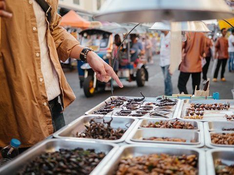 man in a market in front of bowls with different edible insects symbol for entomophagy