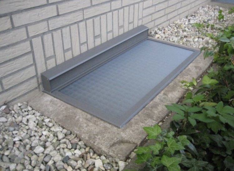 Regenschutzabdeckung für Lichtschacht aus Aluminium, passgenau montiert vor Kellerfenster