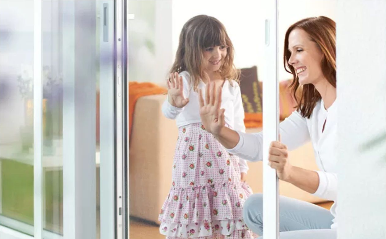 Niña y madre junto a una puerta corredera con mosquitera de ISK Systeme – solución cómoda y segura para puertas de terraza o balcón.