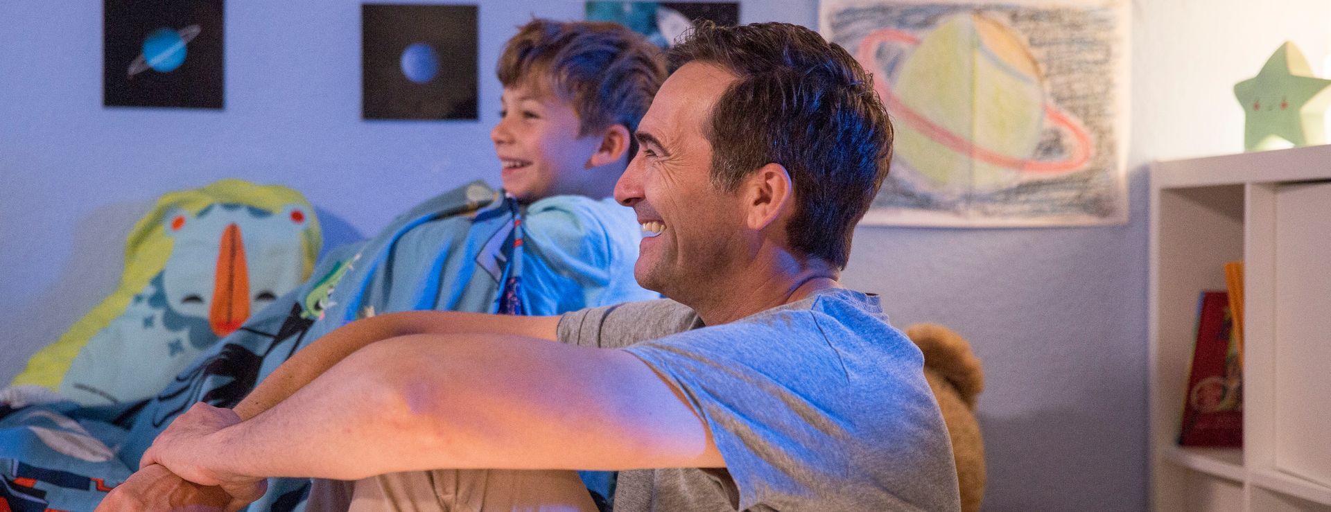 Padre e hijo sentados tranquilamente por la noche en la habitación infantil, disfrutando de un ambiente relajado y sin insectos gracias a la protección antimosquitos.