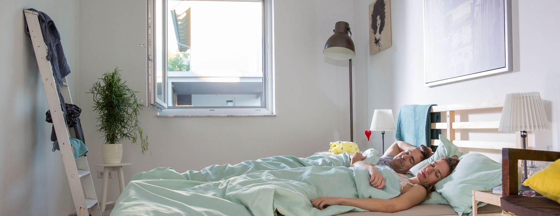 Pareja durmiendo tranquilamente con la ventana abierta, protegidos de insectos y polen gracias al tejido Polltec®, para un descanso reparador.