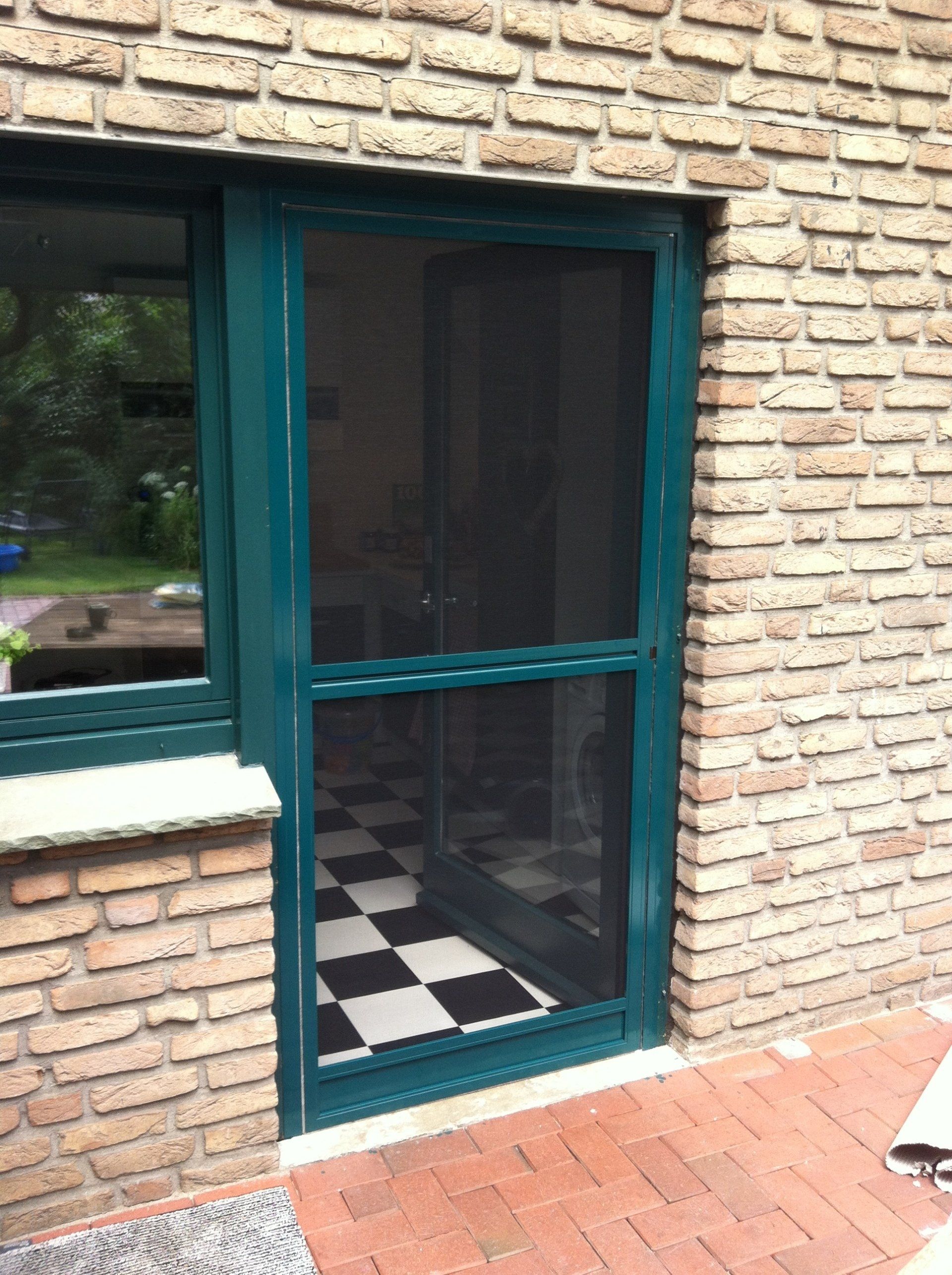 Puerta abatible con mosquitera en marco de aluminio oscuro – protección eficaz para accesos exteriores