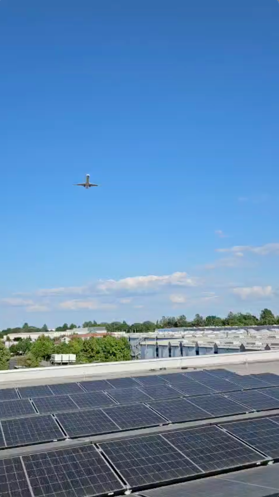 Flugzeug über Industrieanlage mit Photovoltaikanlage auf dem Dach – Symbol für nachhaltige Energie u