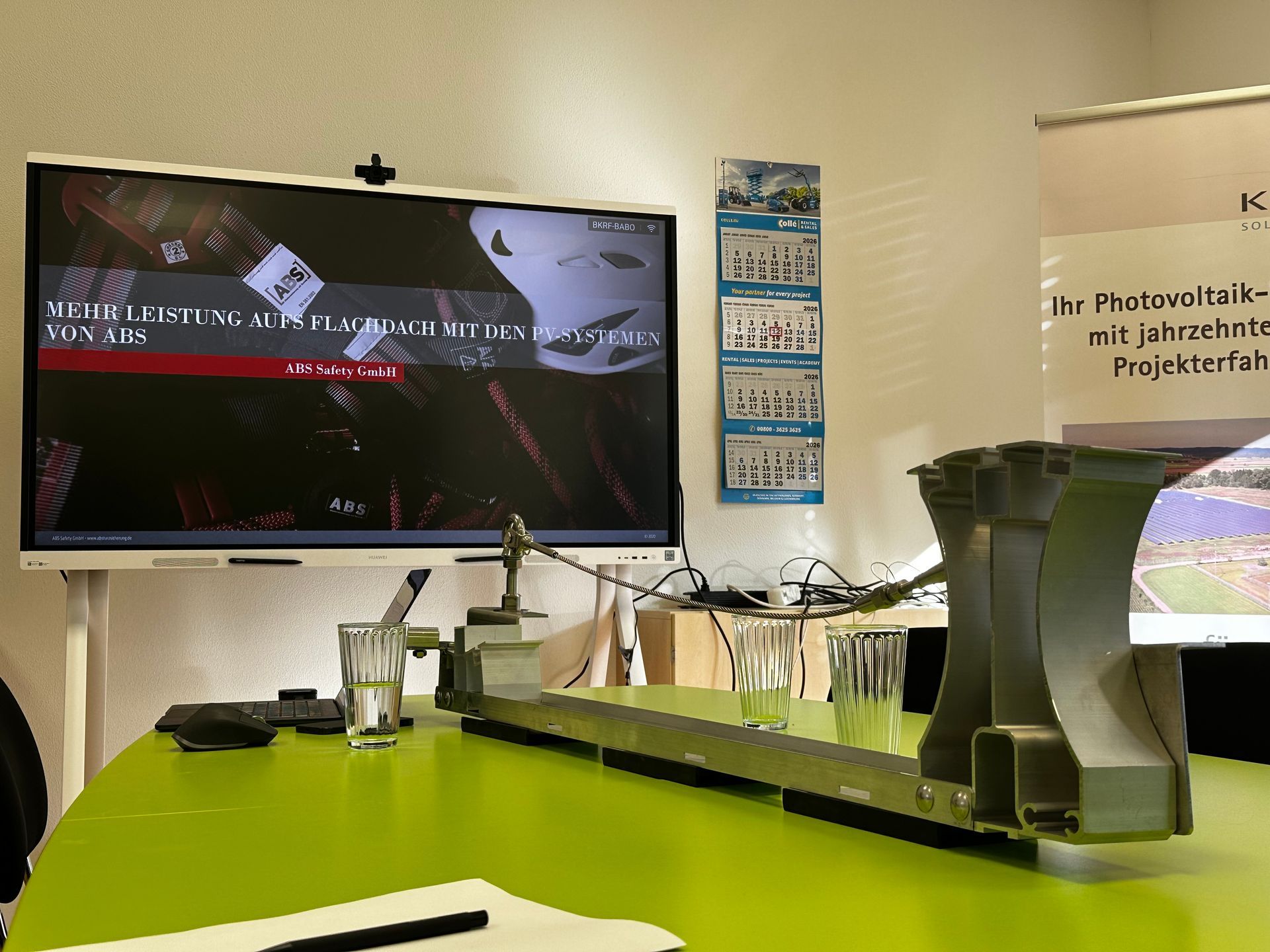 Konferenztisch mit technischen Bauteilen, Präsentation zu Dachsystemen auf Bildschirm und Kalender
