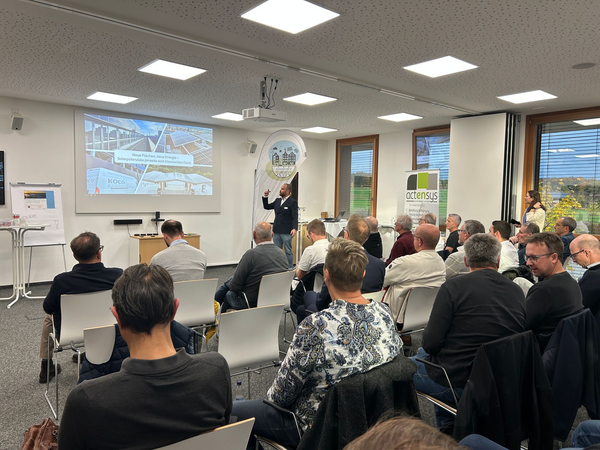 Vor einem Publikum hält ein Redner in einem hellen Konferenzraum eine Präsentation zum Thema Solarpo