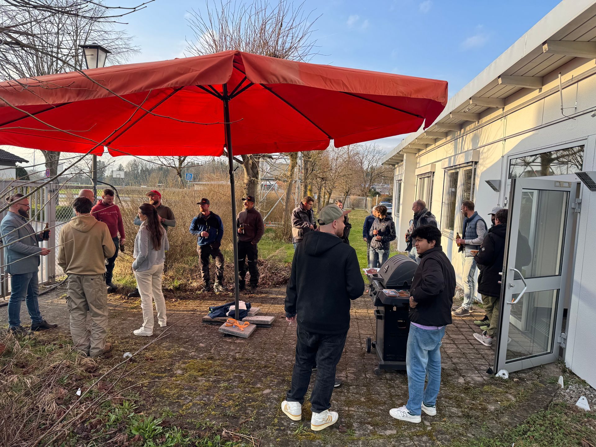 Kollegen genießen Grillabend im Freien bei Sonne, Getränken und guter Stimmung