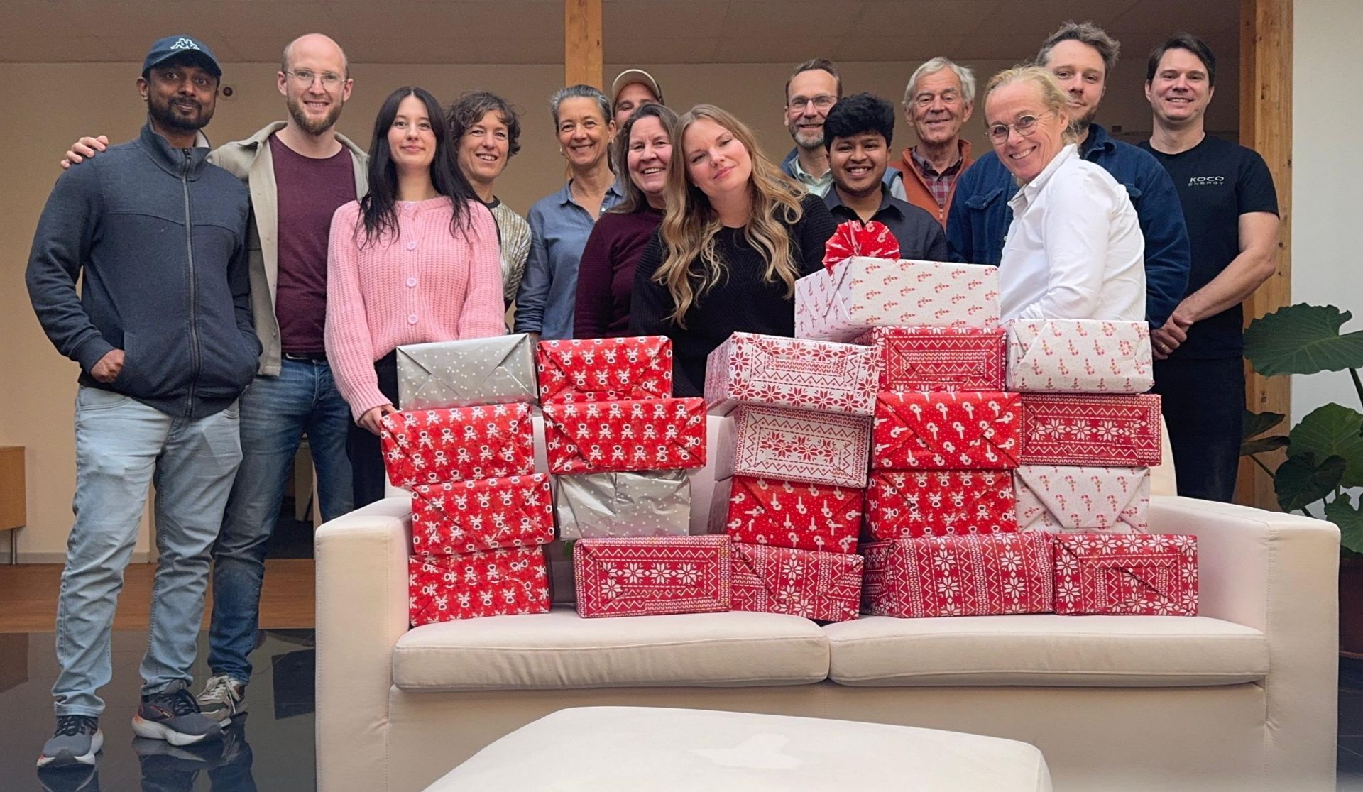 Team KOCO Energy mit vielen weihnachtlich verpackten Spendenkartons auf einem Sofa bei der Aktion We