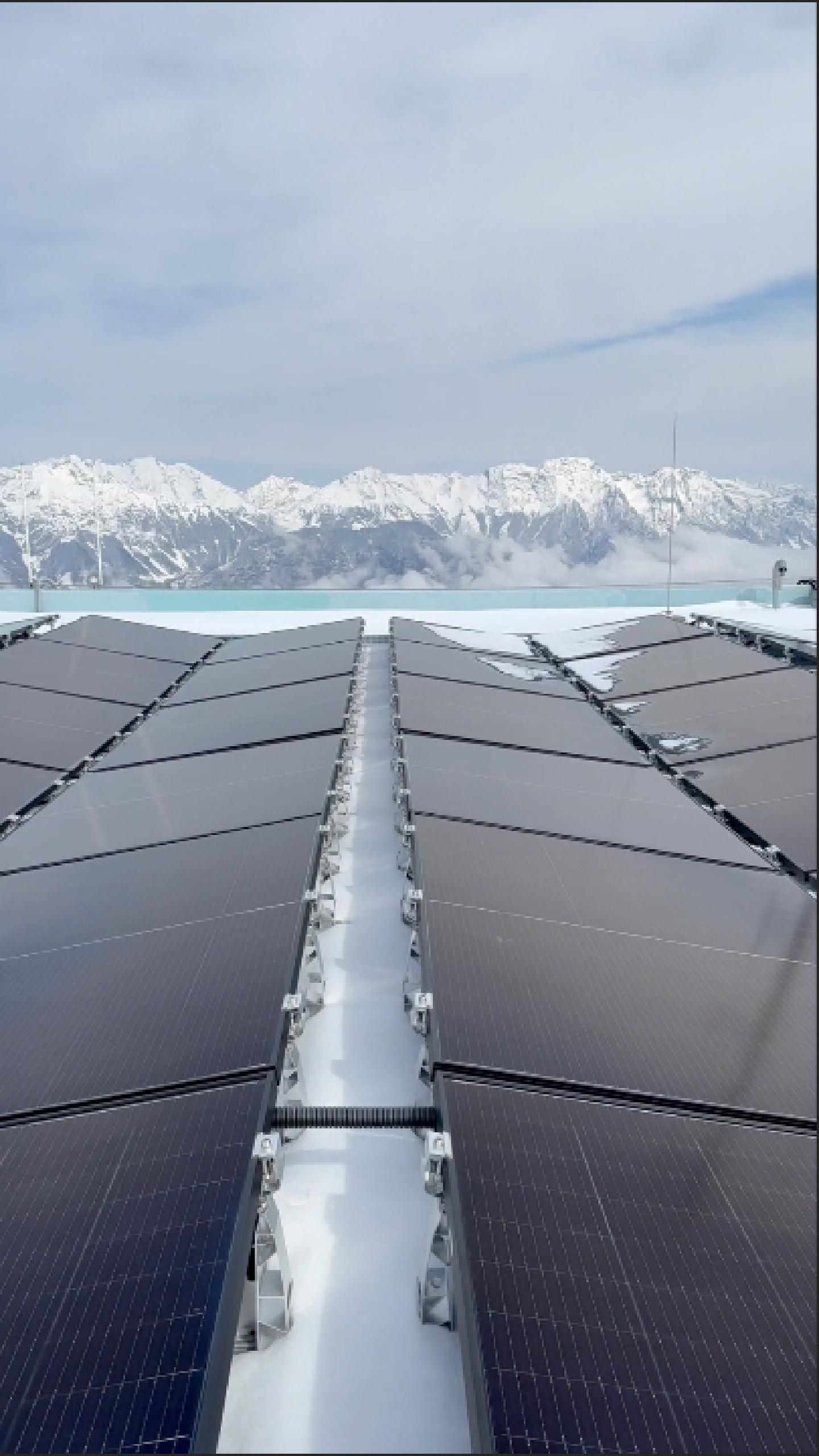 PV‑Module auf verschneitem Flachdach mit klarer Sicht auf die umliegende alpine Berglandschaft